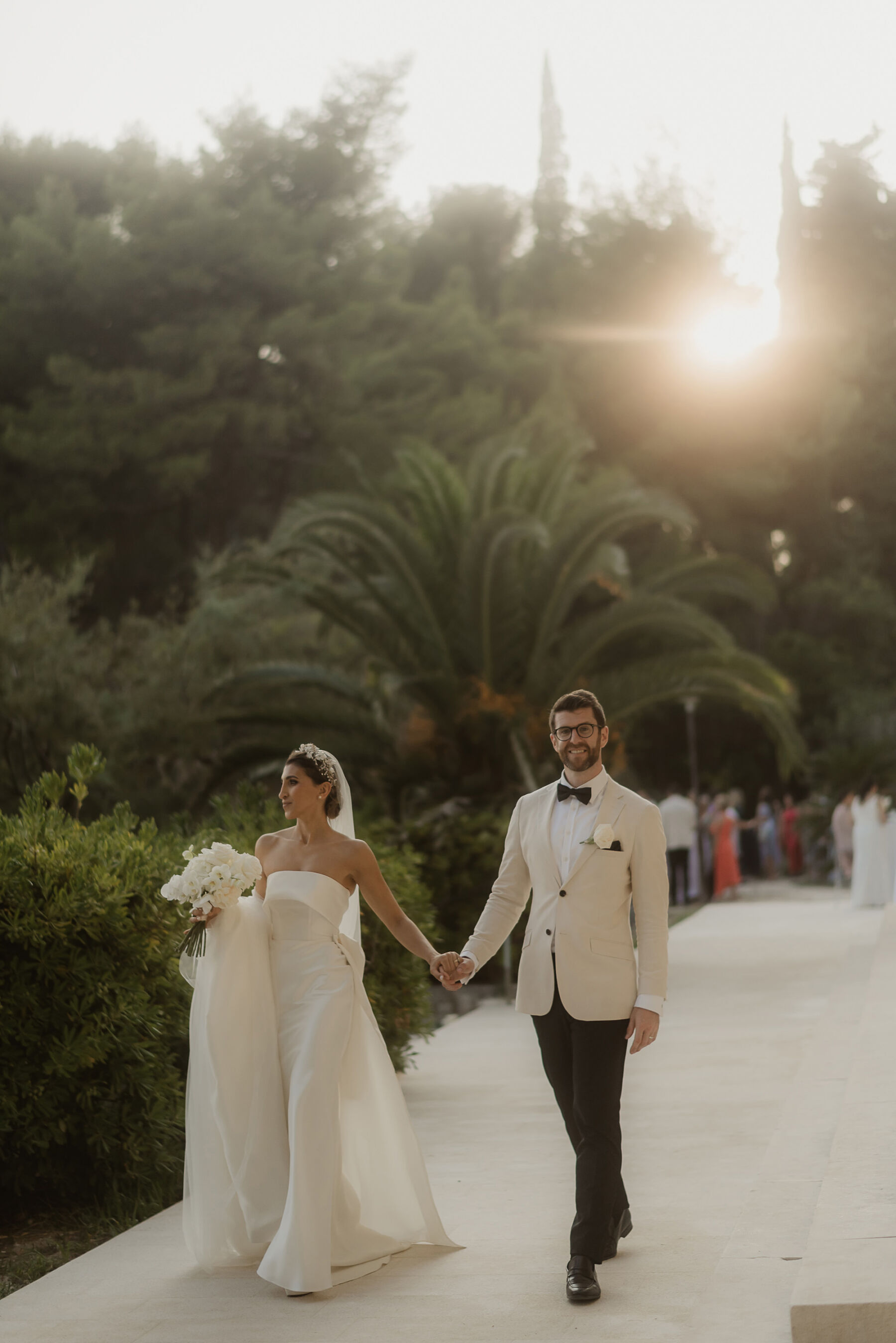 Groom in white tux holding hands with bride in minimalist wedding dress by Eva Lendel