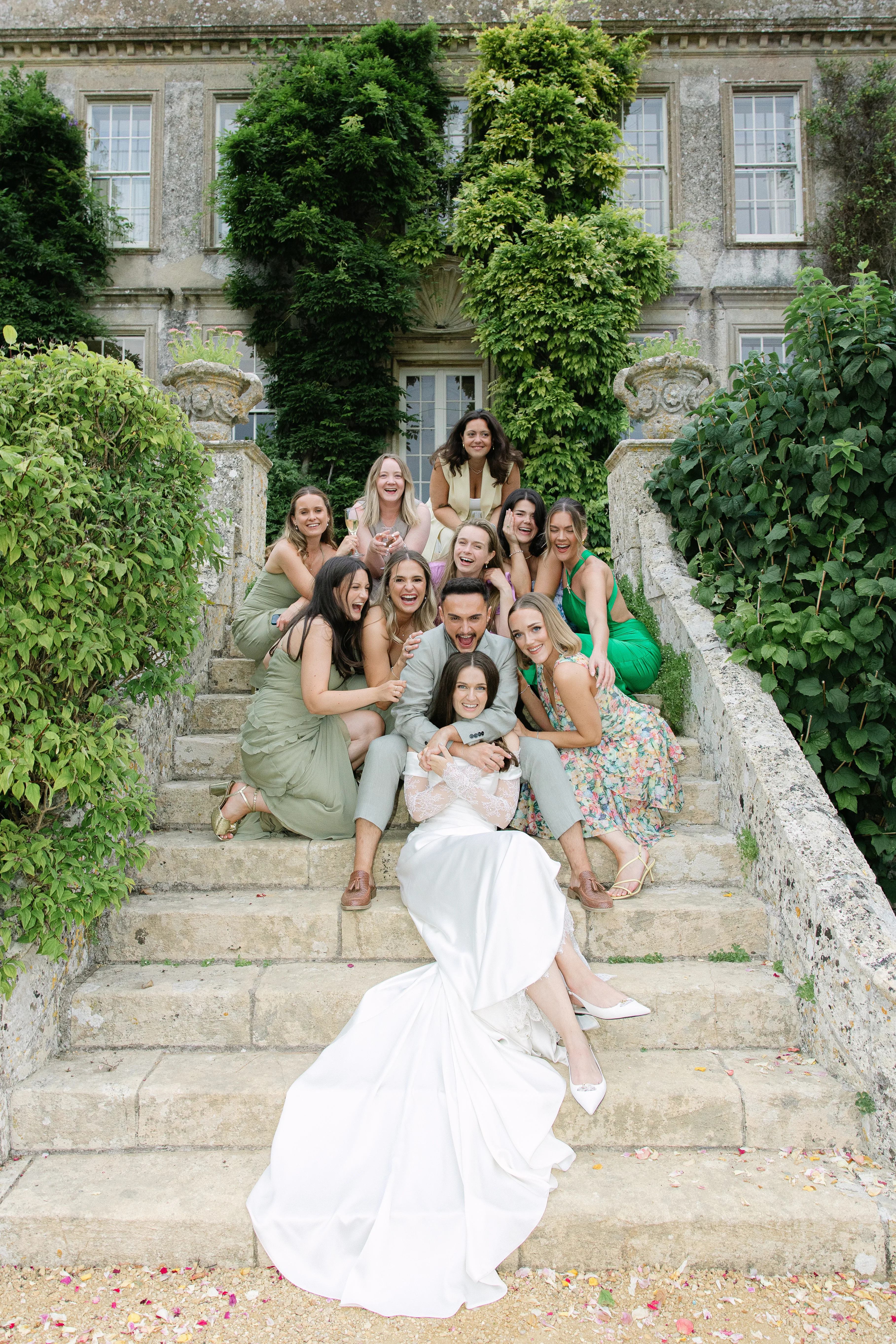 Editorial group shot, group of wedding guests and bride on steps laughing and feeling relaxed
