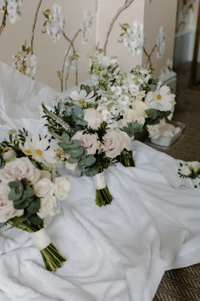 Three bridal bouquets are lined up waiting to be carried down the aisle. Each full of roses, foliages and cosmos in green and white.