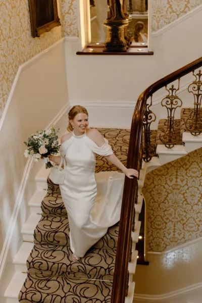 A bride descends a staircase whilst holding her bouquet of flowers.