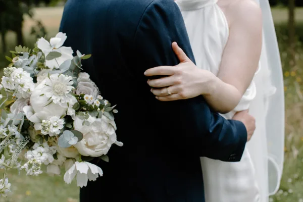 A close up of a bride & groom embracing. The image just shows the back of the groom and the brides bouquet.