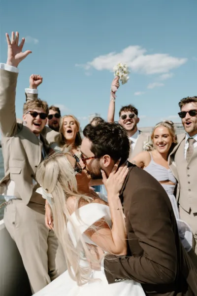 bride groom kissing while friends cheer behind London Trinity Bouy Wharf wedding