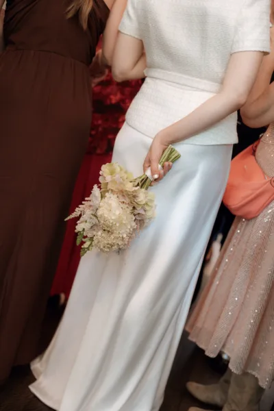 A close up image of a bride holding her bouquet of hydrangea and snapdragons behind her back.