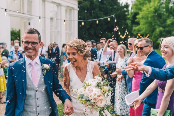 A bride & Groom showered in confetti as they walk out of the orangery at Gunnersbury Park House