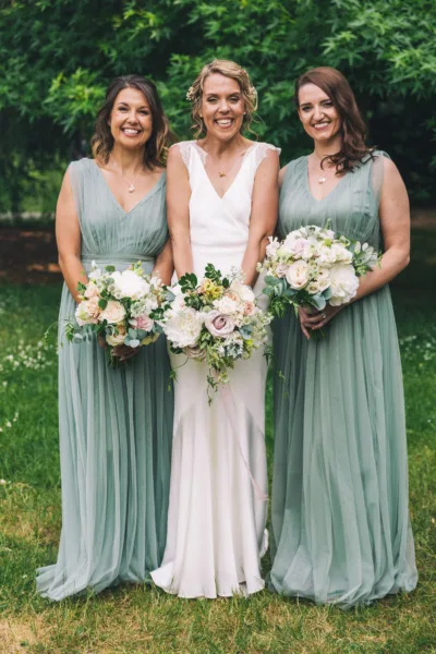 A bride and her two bridesmaids pose for a photo holding their bouquets in the garden of Gunnersbury Park.