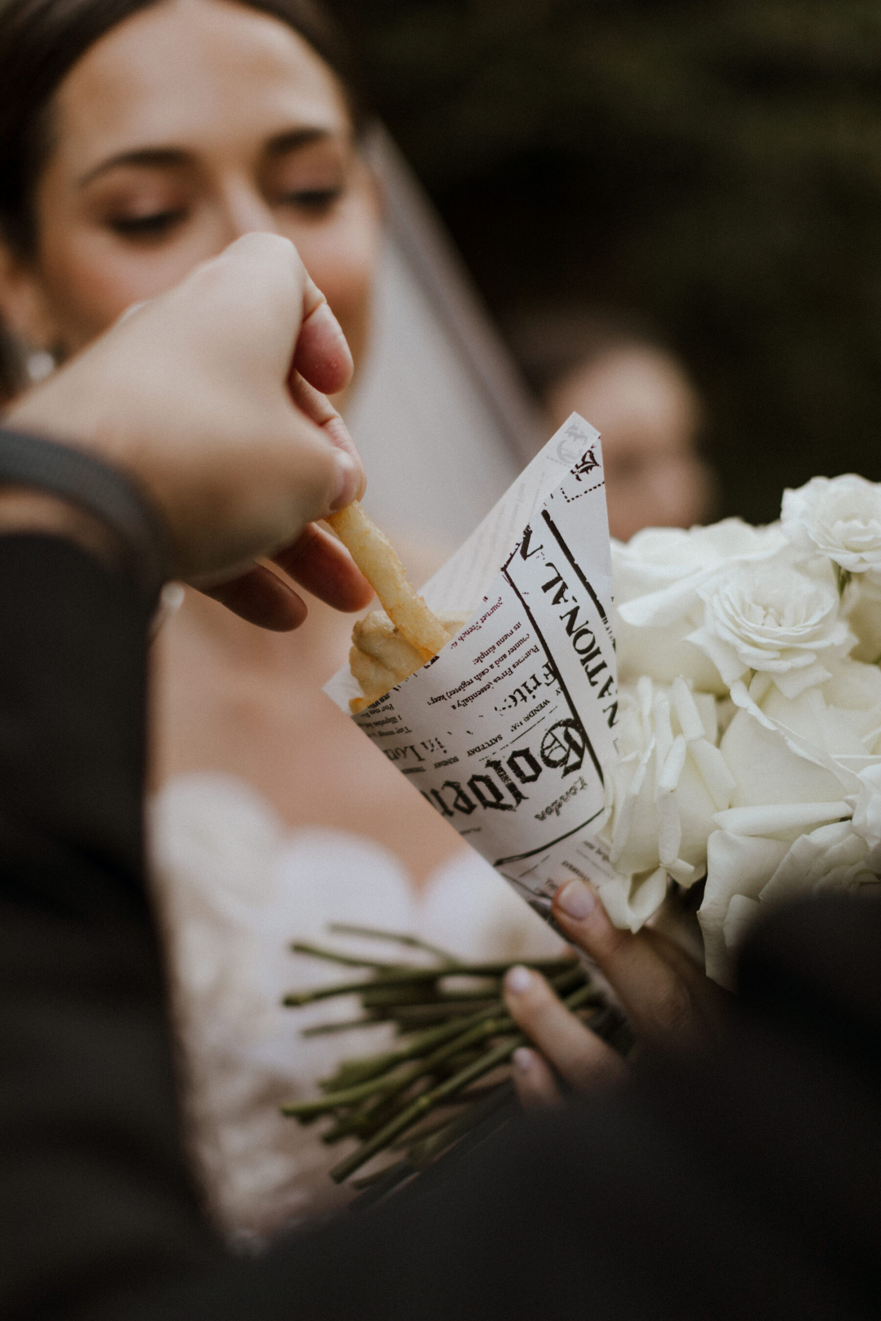 Bride and groom eating mini fish and chips from a newspaper cone.