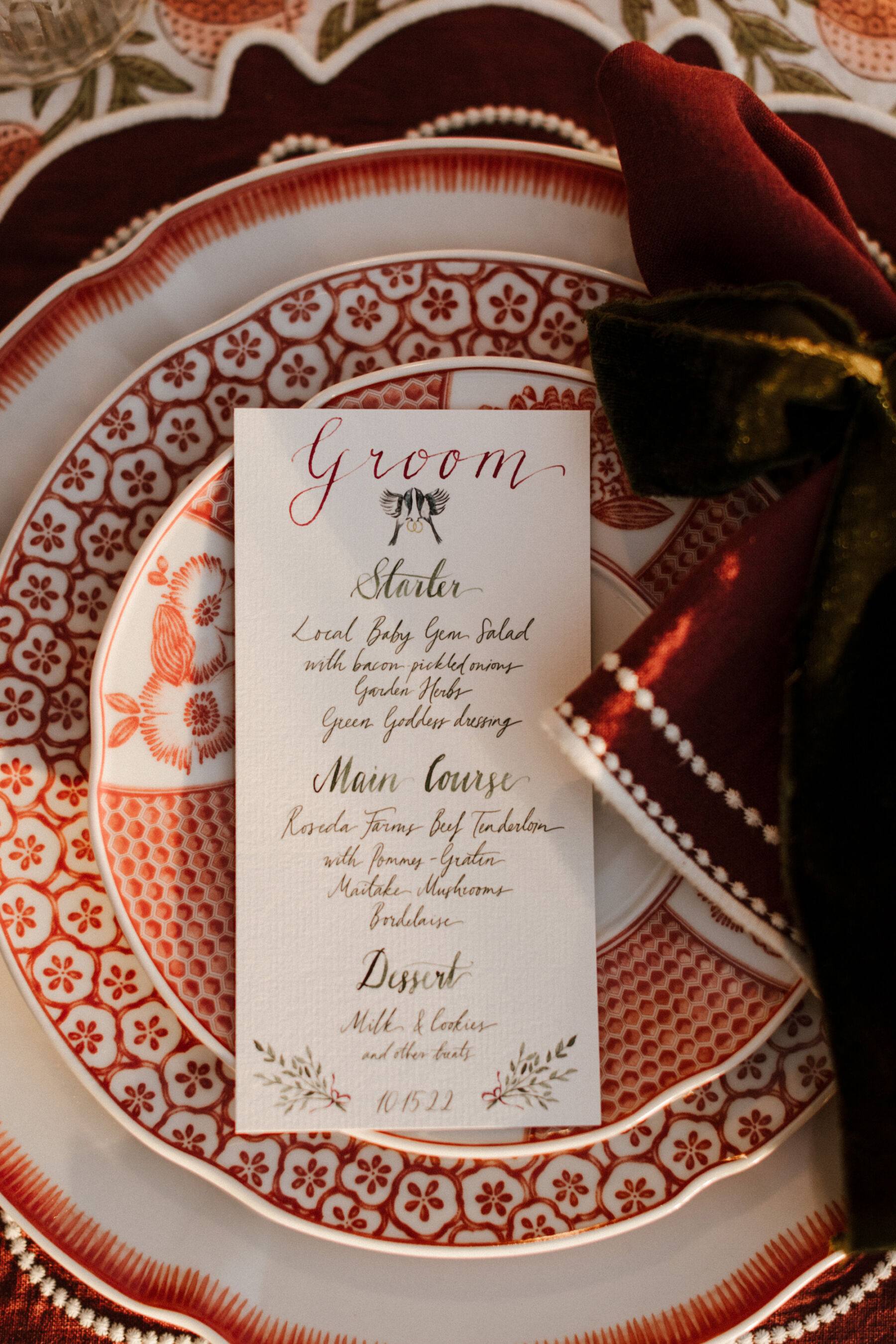 Hand calligraphy written wedding menu personalised for each guest featuring a wedding logo of two birds holding rings.