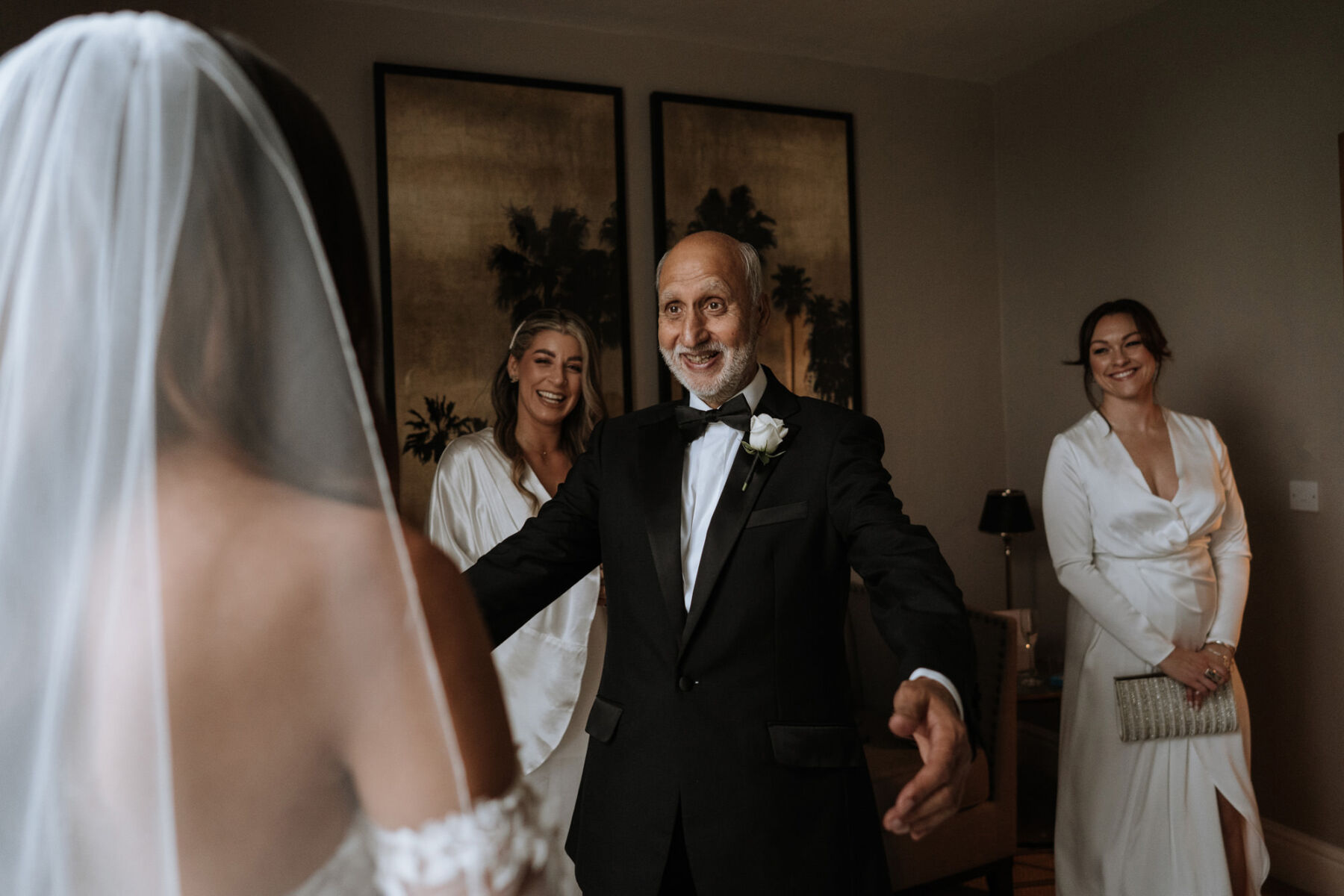 Father of the bride in black tie sees his daughter for for first time in her wedding dress and looks surprised and happy