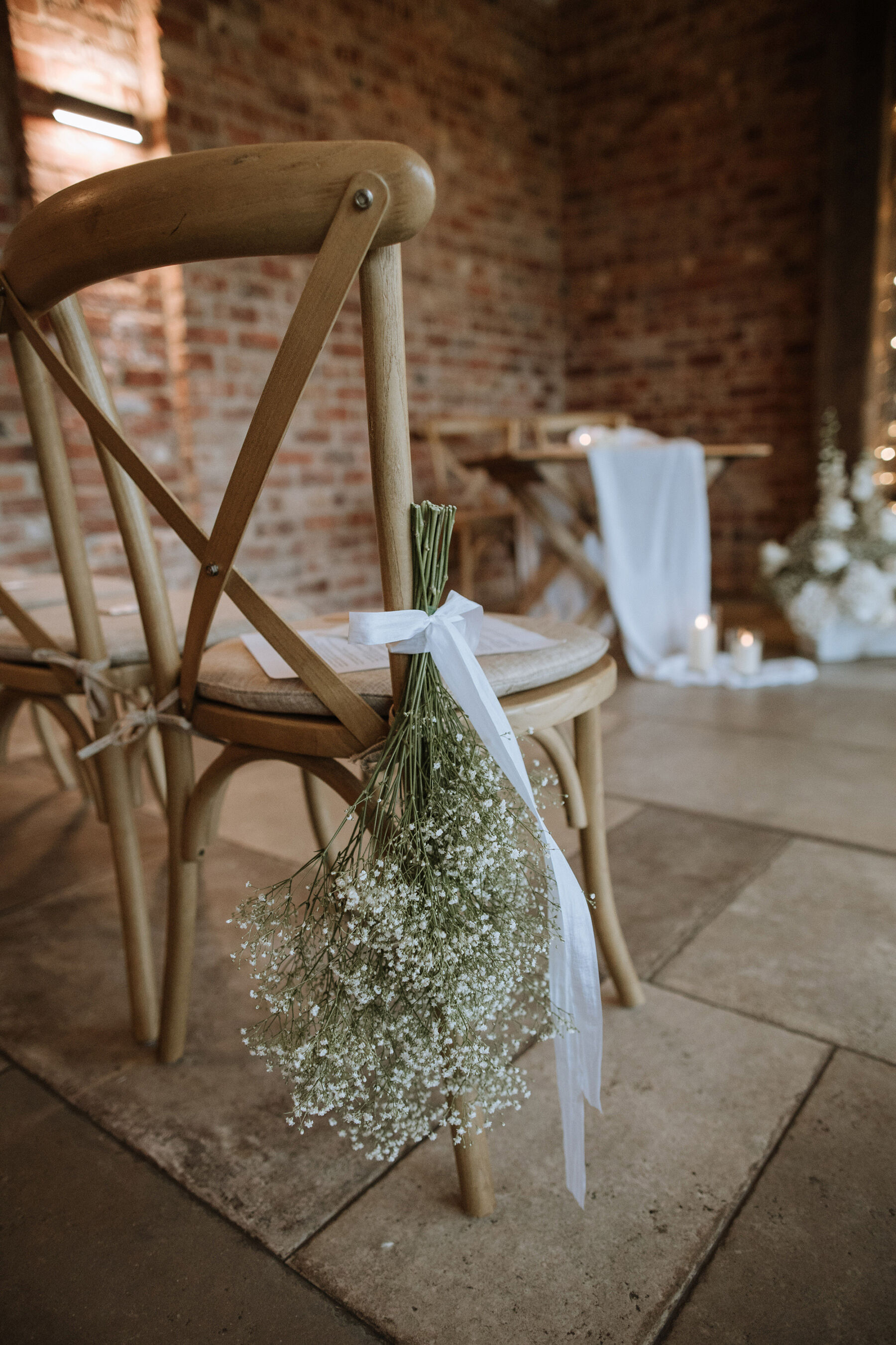 Gypsophila tied with ribbon to wooden crossback chairs.