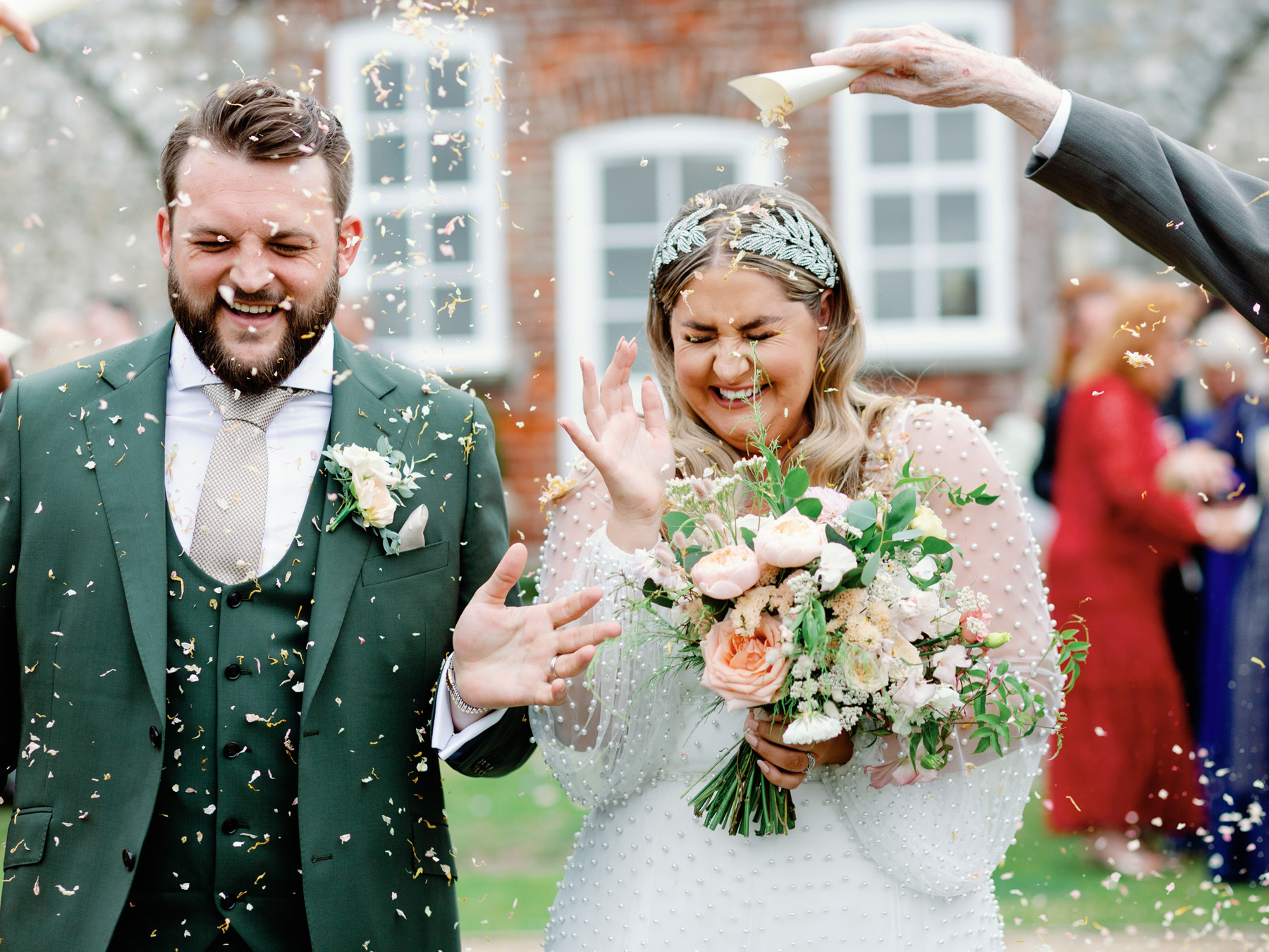 Bride and groom in a confetti shower. Bride holds a peach bouquet and wears a dress covered with pearls.