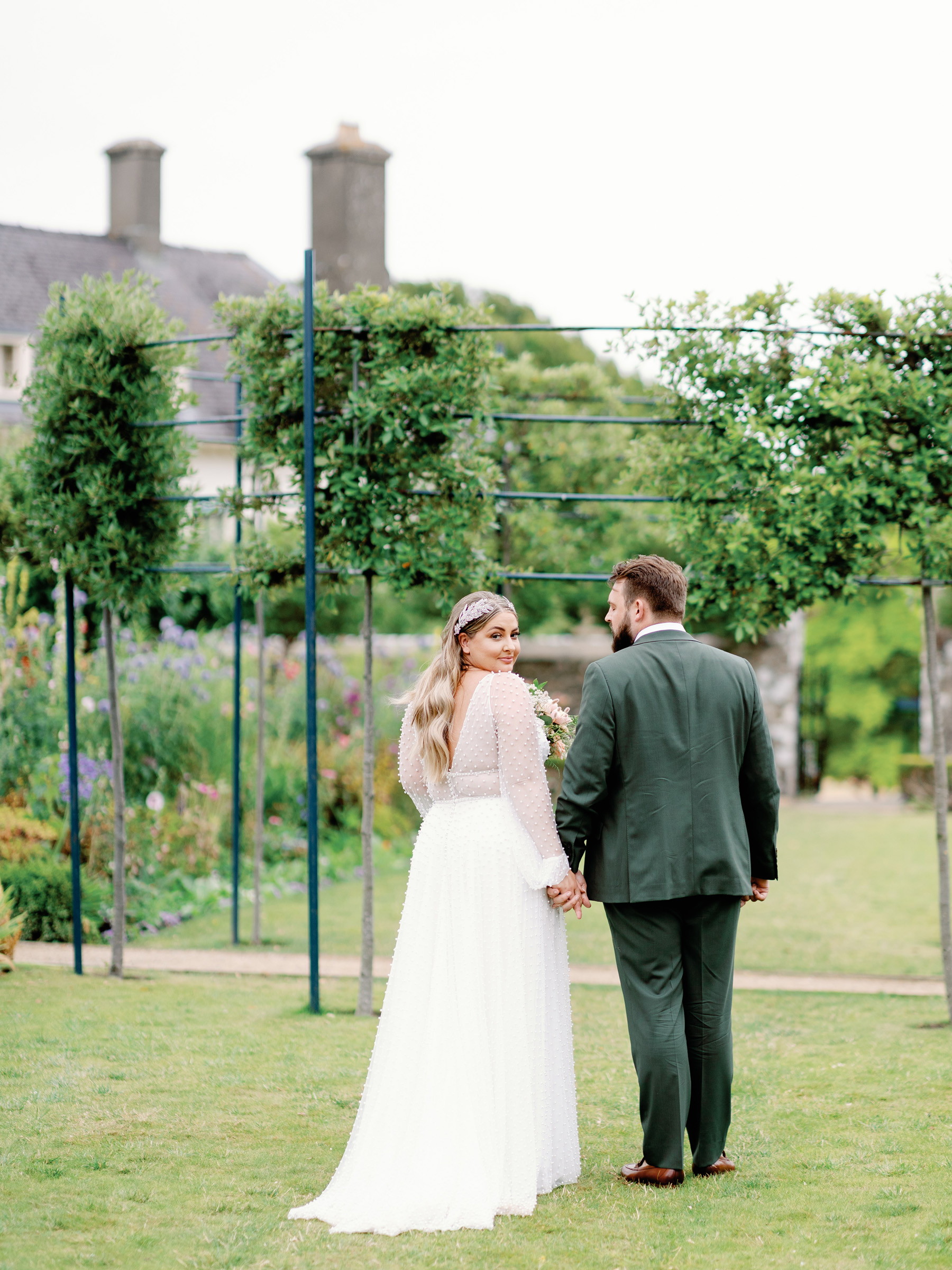 Behind shot of bride and groom, bride is turning back to look at the camera, she wears a dress covered in pearls. 