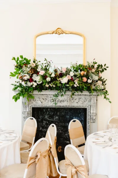 A mantel above a fireplace in Pembroke lodge is full of foliage and flowers in pale pink, ivory and burgundy. Ready for a wedding reception.