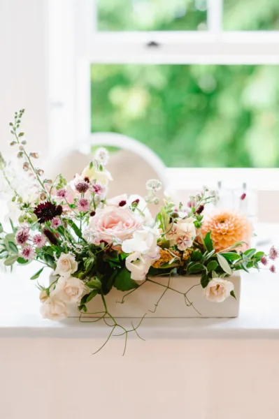 A small ceramic vase full of flowers catching the light as it sits on the ceremony table at Pembroke Lodge.