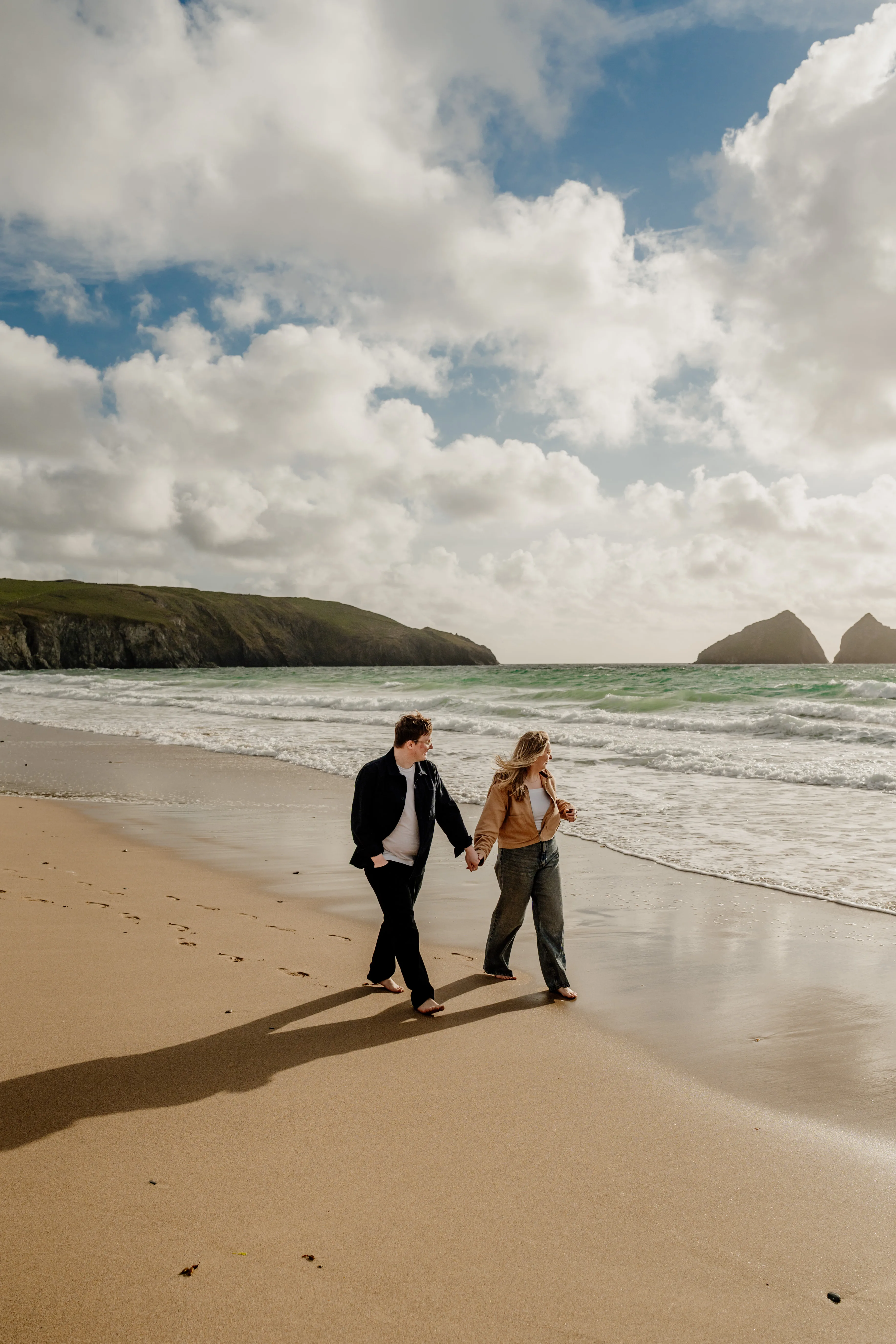 Couple walking along Holywell Bay during engagement shoot with ryan goold photography
