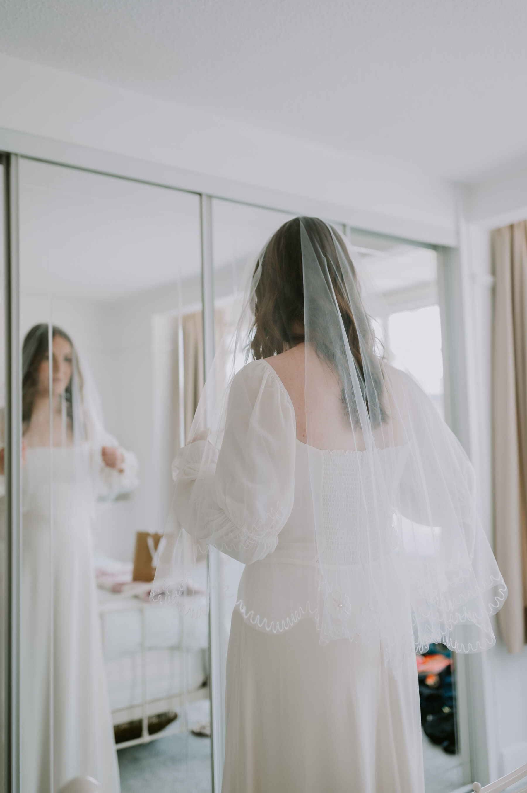 Bride in a Reformation wedding dress looking at elbow length wedding veil.