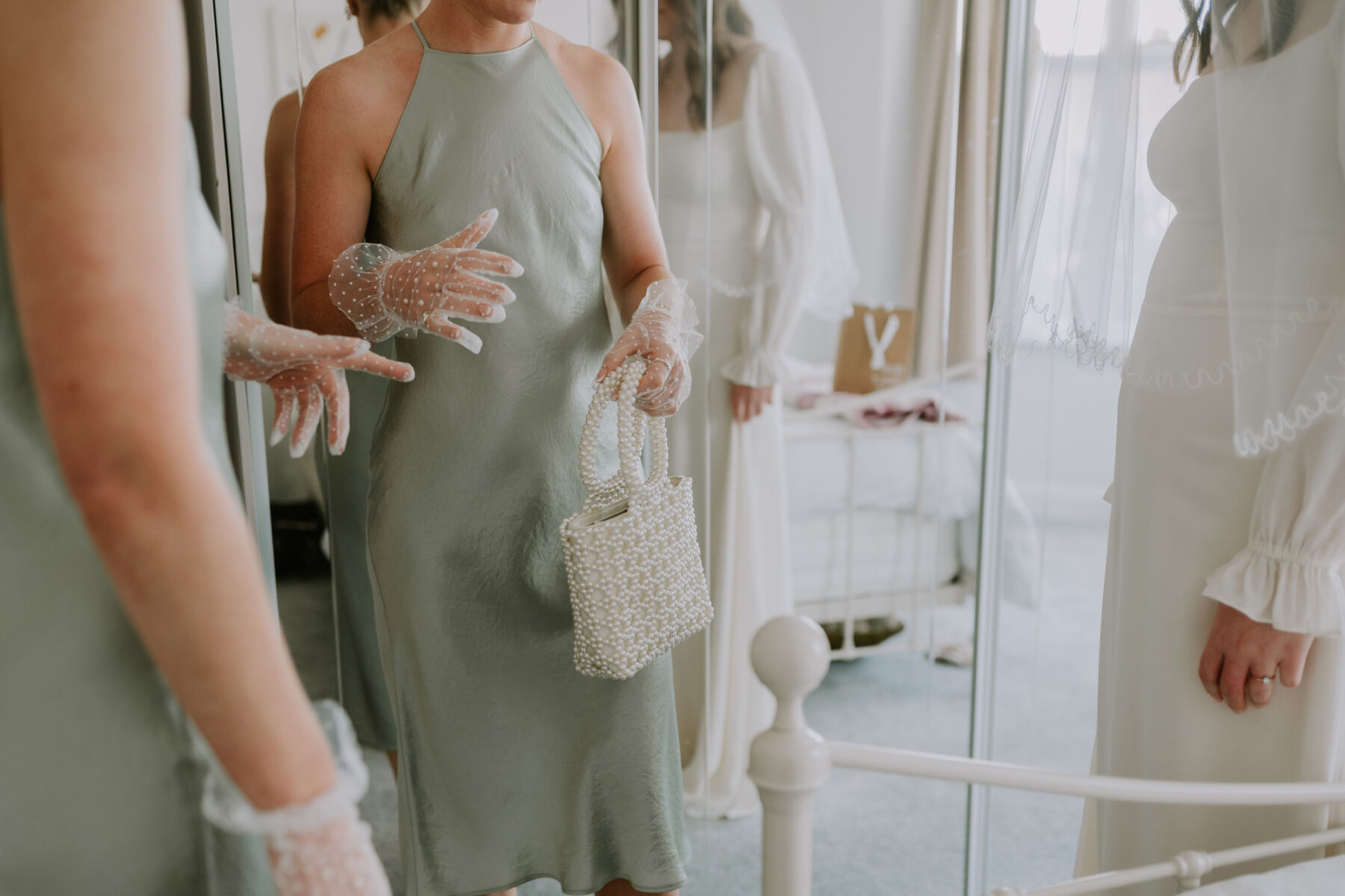 Bridesmaid in green slip dress holding a pearl clutch bag. Polka Dot tulle white gloves.