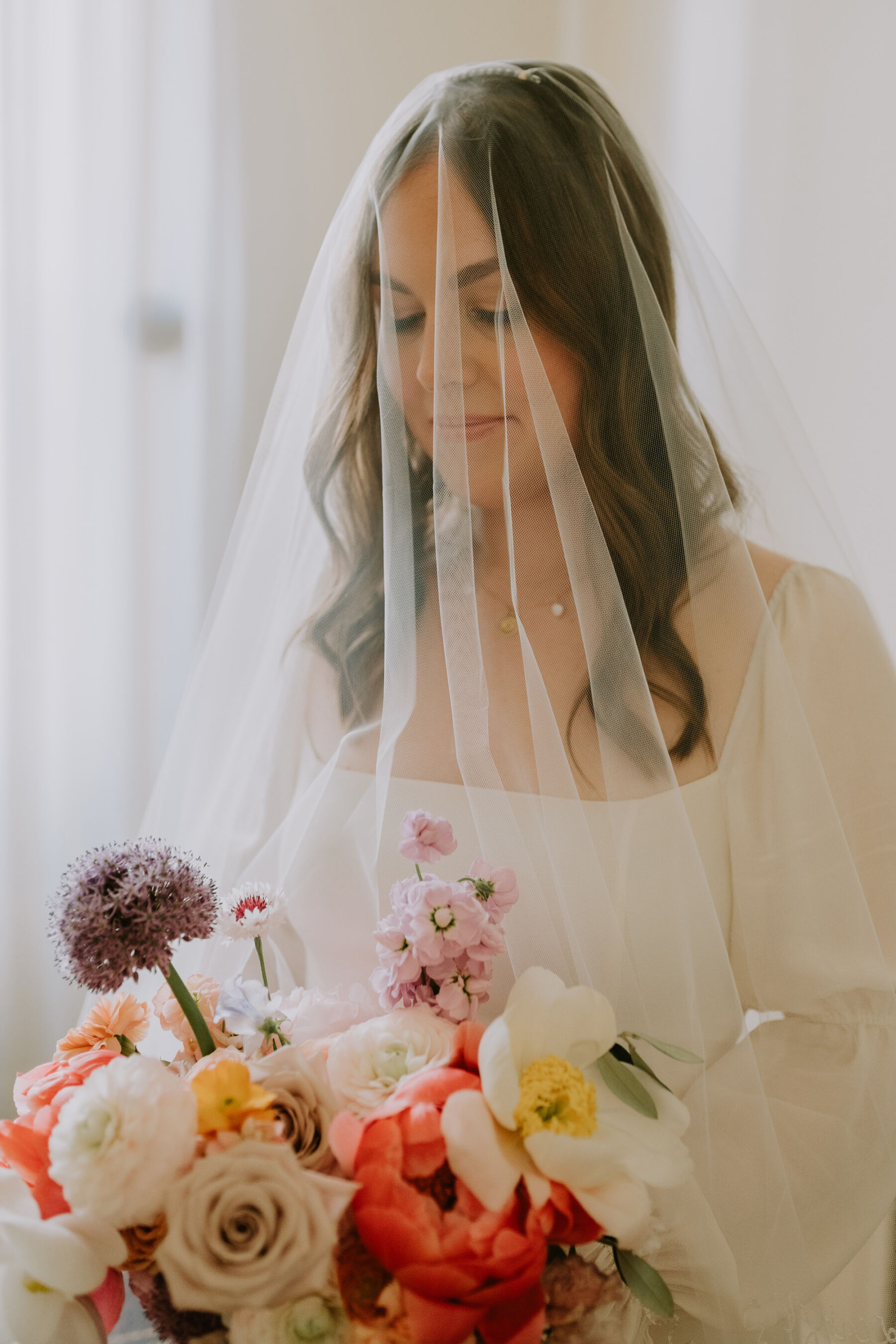 Portrait shot of bride wearing blusher veil and carrying a colourful bouquet. 