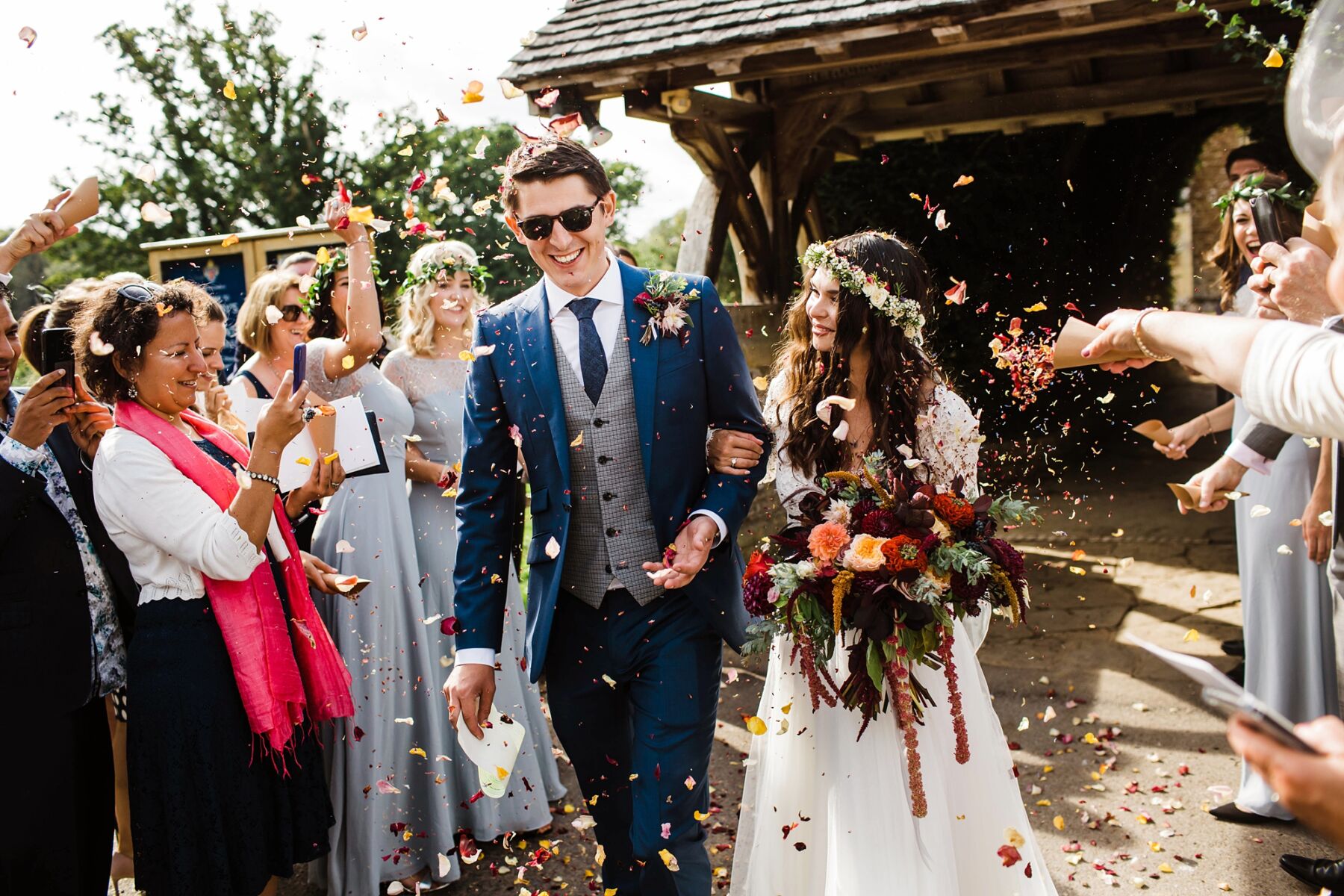 Bohemian bride with a beautiful oversized Autumn wedding bouquet and flower crown, in arms with her groom in a shower of confetti, by Claudia Rose Carter Photography.