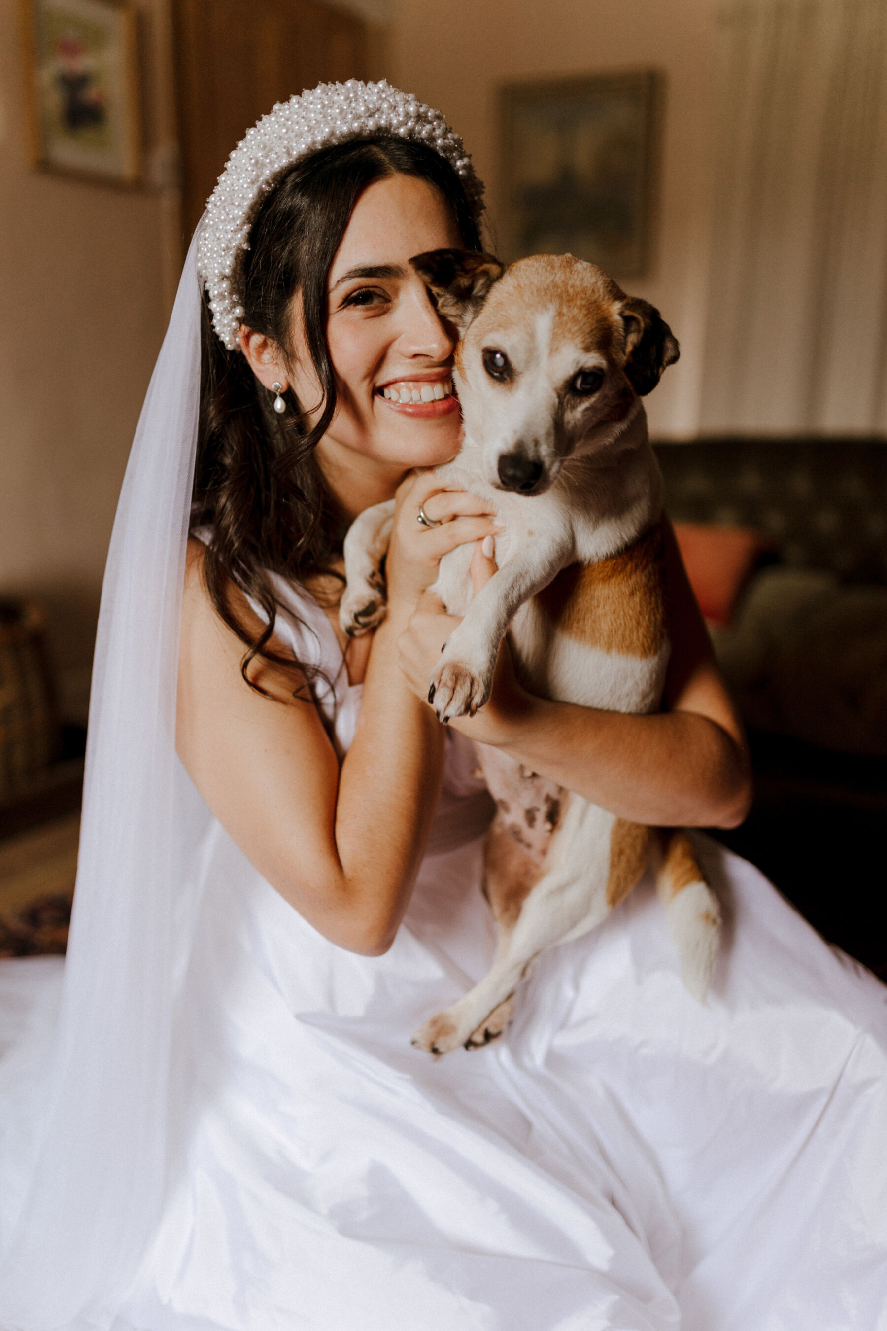 Bride wearing a pearl headband, veil and a Jessica Bennett wedding dress whilst holding her little dog on her lap.