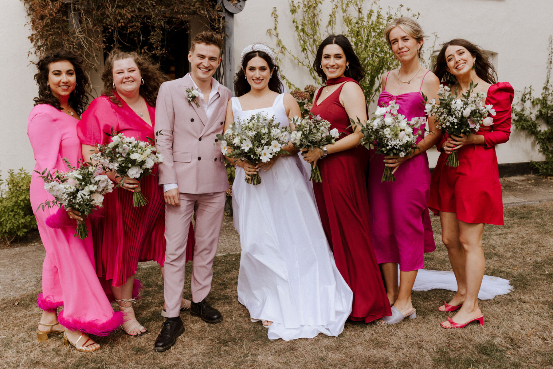 Bridesmaids in bright red and pink dresses. Male bridesmaid in a pale pink suit.