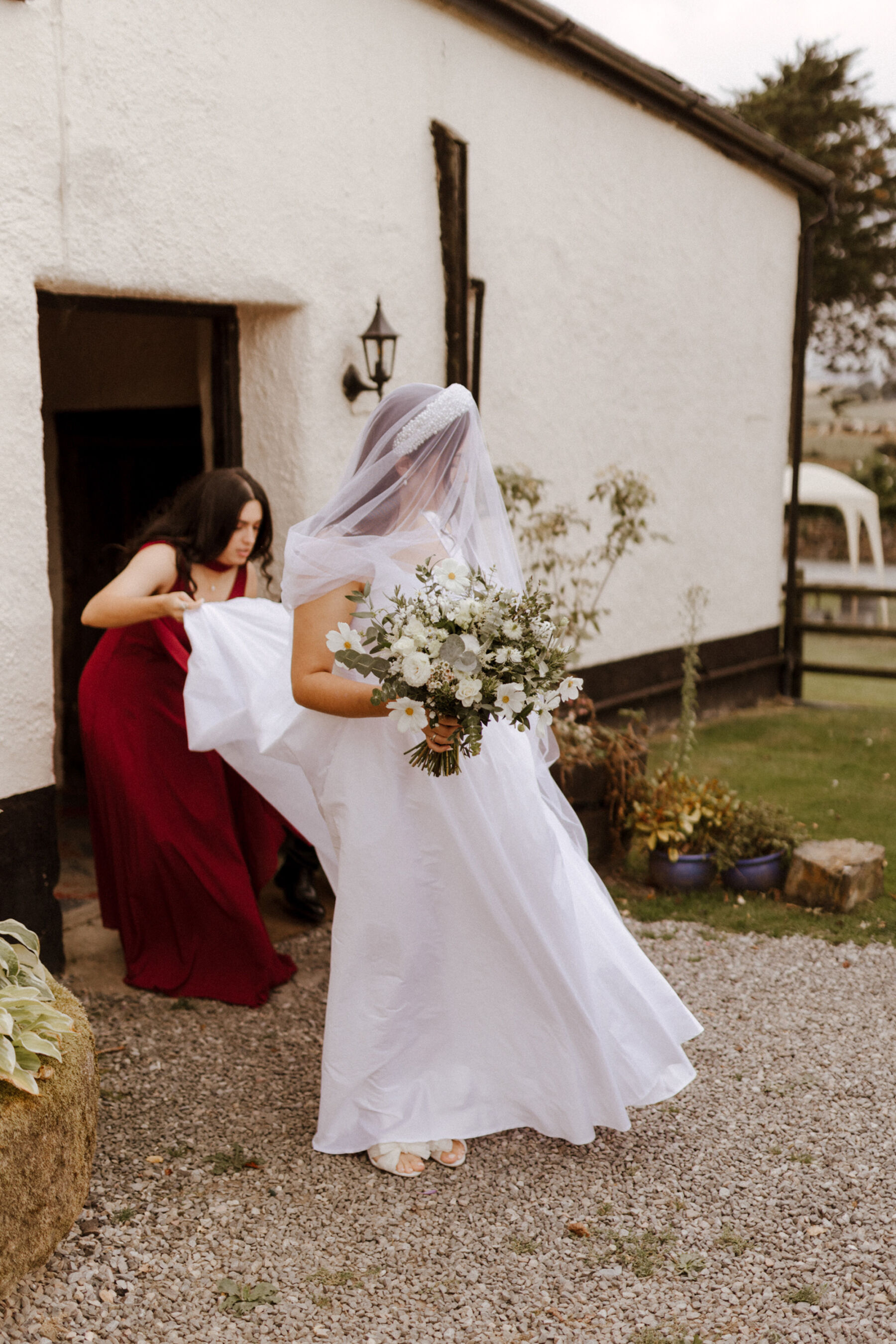 Bride with her face covered with a veil being escorted to the wedding ceremony whilst holding a large bouquet of all white flowers.