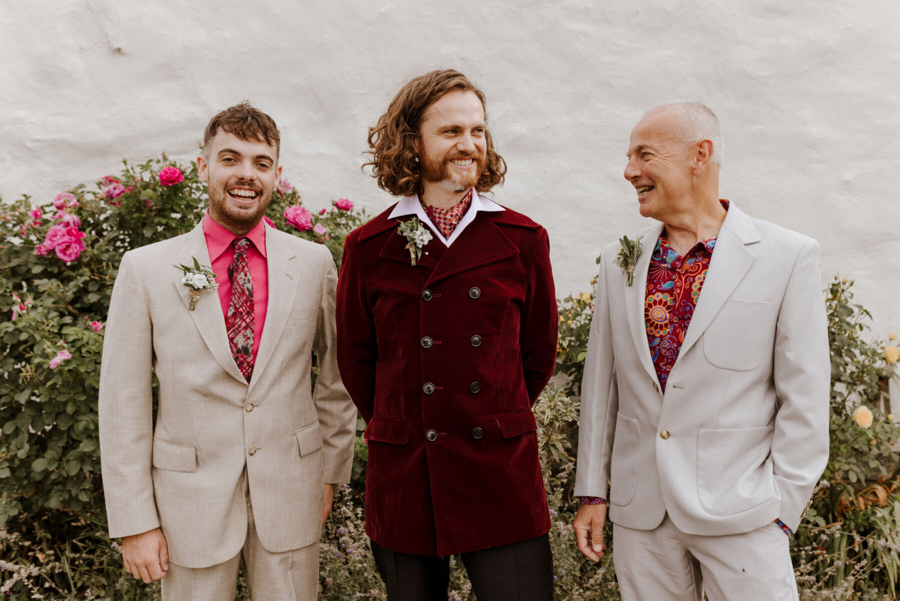 Groom with long wavy hair wearing a 1970's inspired maroon velvet suit.