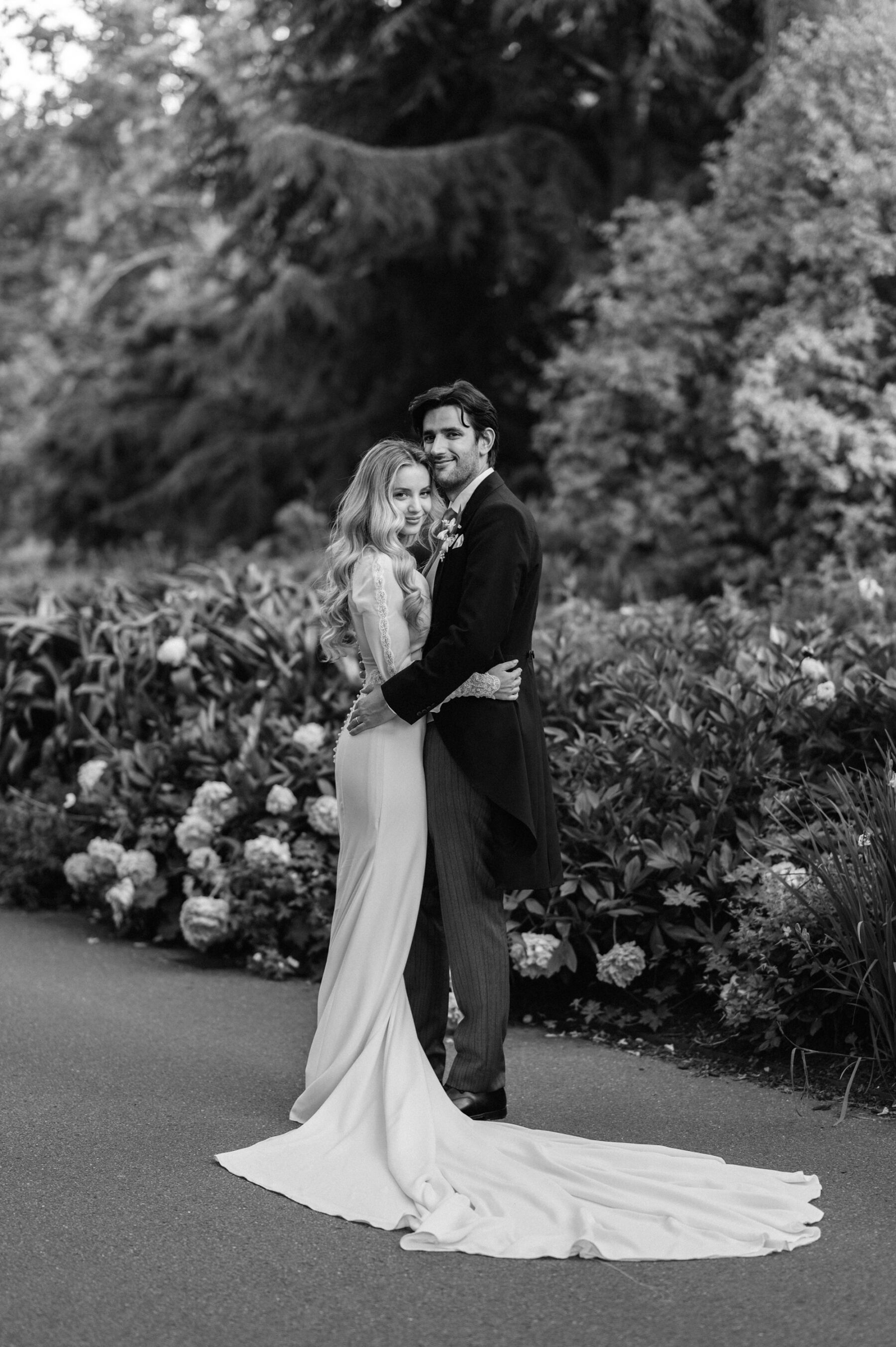 Black and white shot of bride and groom embracing in a garden. Bride wears Rosa Clara wedding dress.