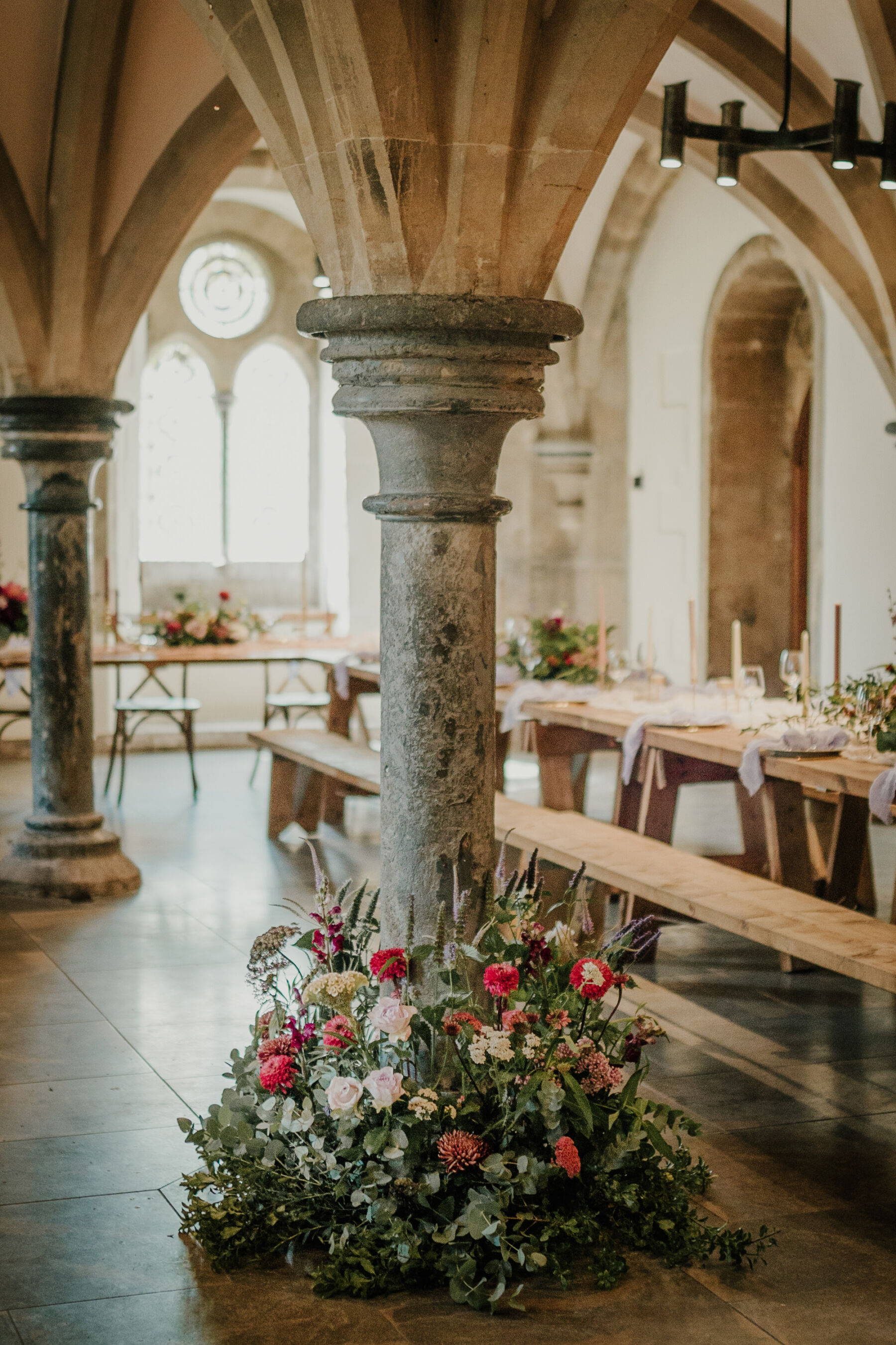 Beautiful read flowers adoring a stone pillar inside Bishop's Palace historic wedding venue in Wells, Somerset.