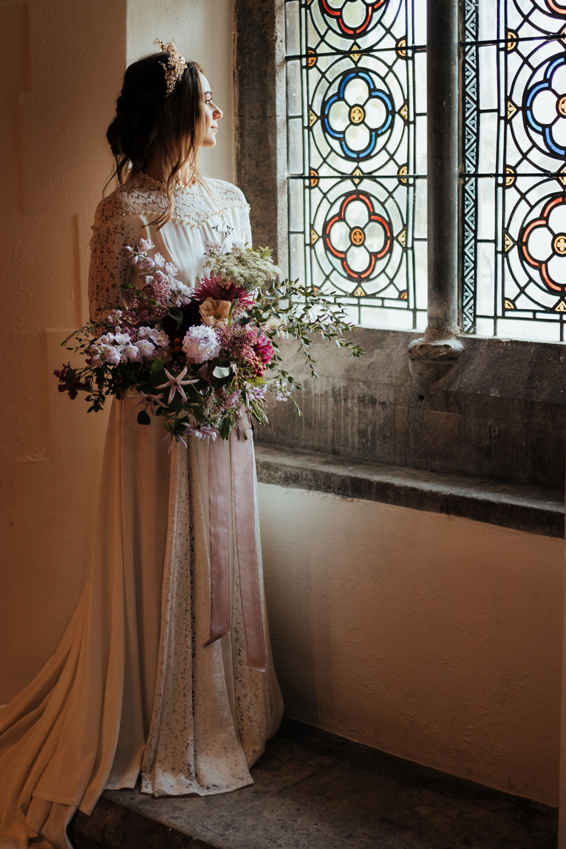 Bride wearing a vintage lace wedding dress and a bridal crown & carrying a large colourful summer bouquet. Bishop's Palace historic wedding venue in Wells, Somerset.