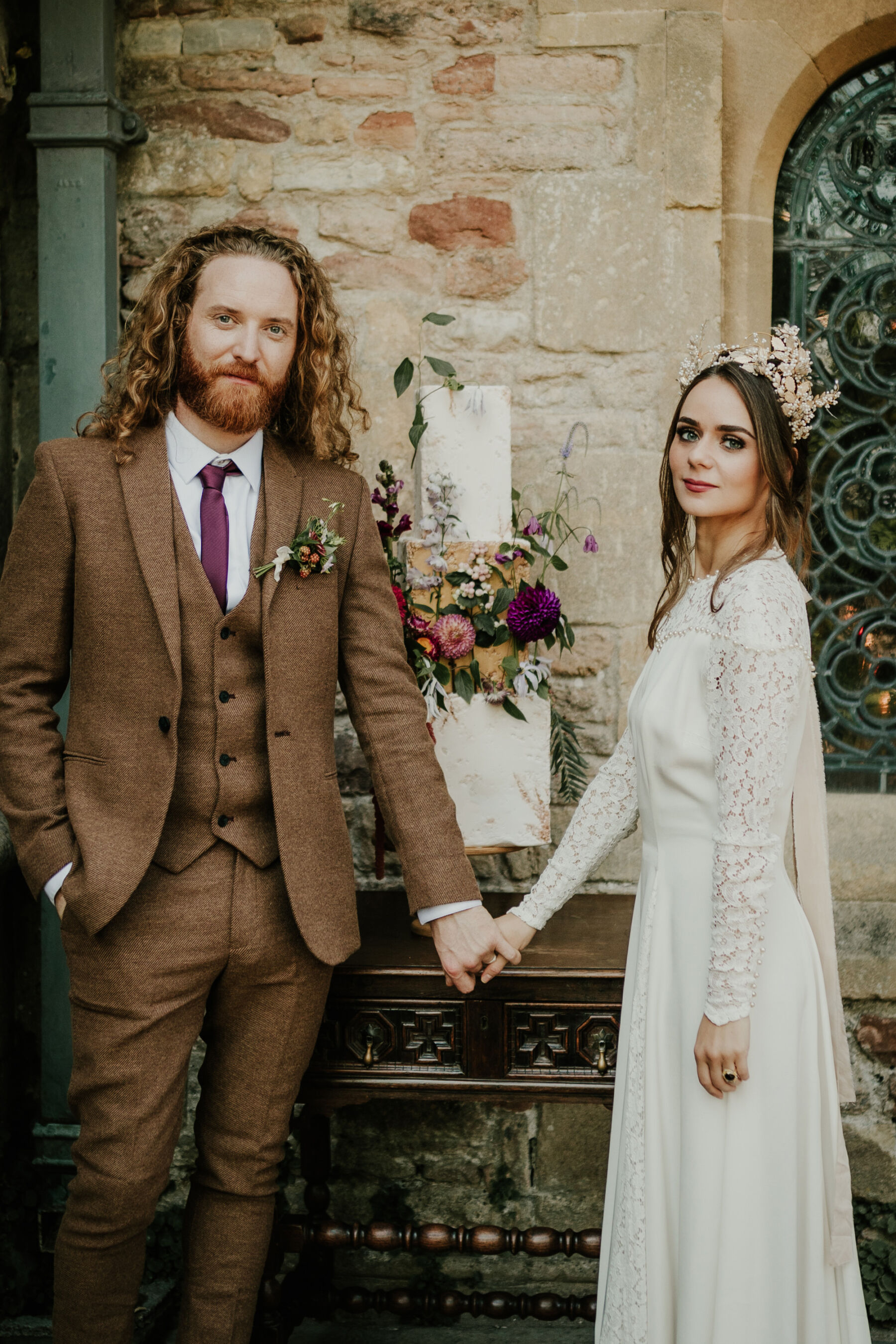 Bride wearing a vintage lace wedding dress and a bridal crown. Groom in a brown suit. Gardens at Bishop's Palace historic wedding venue in Wells, Somerset.