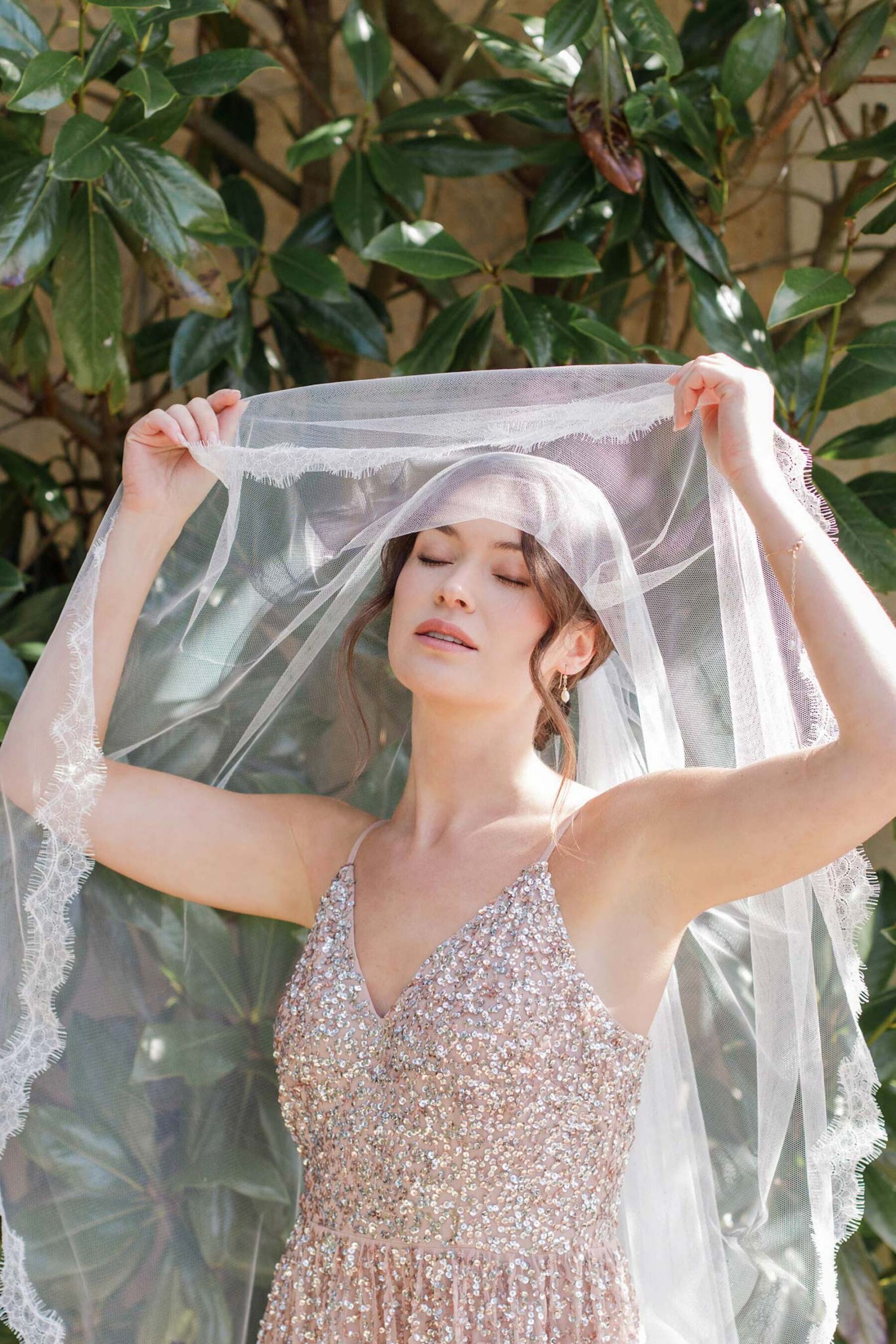 Elegant Lace trim wedding veil by Britten Weddings. Bride lifting the veil to reveal her face.