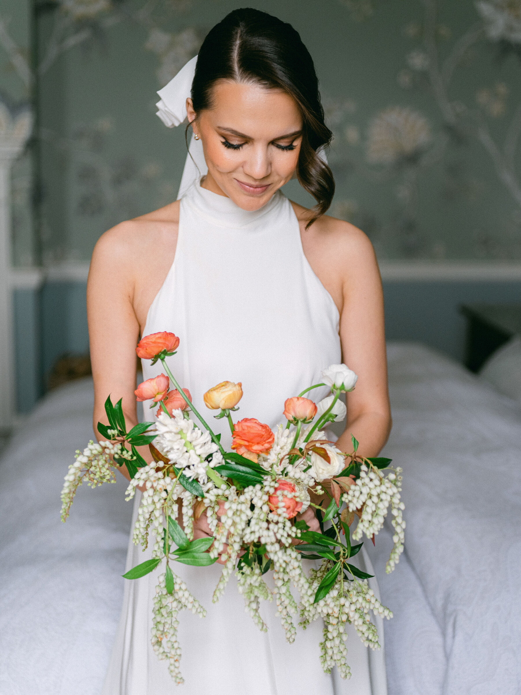 Bride wearing a halterneck wedding dress and looking down to a colourful bouquet of British grown wedding flowers.