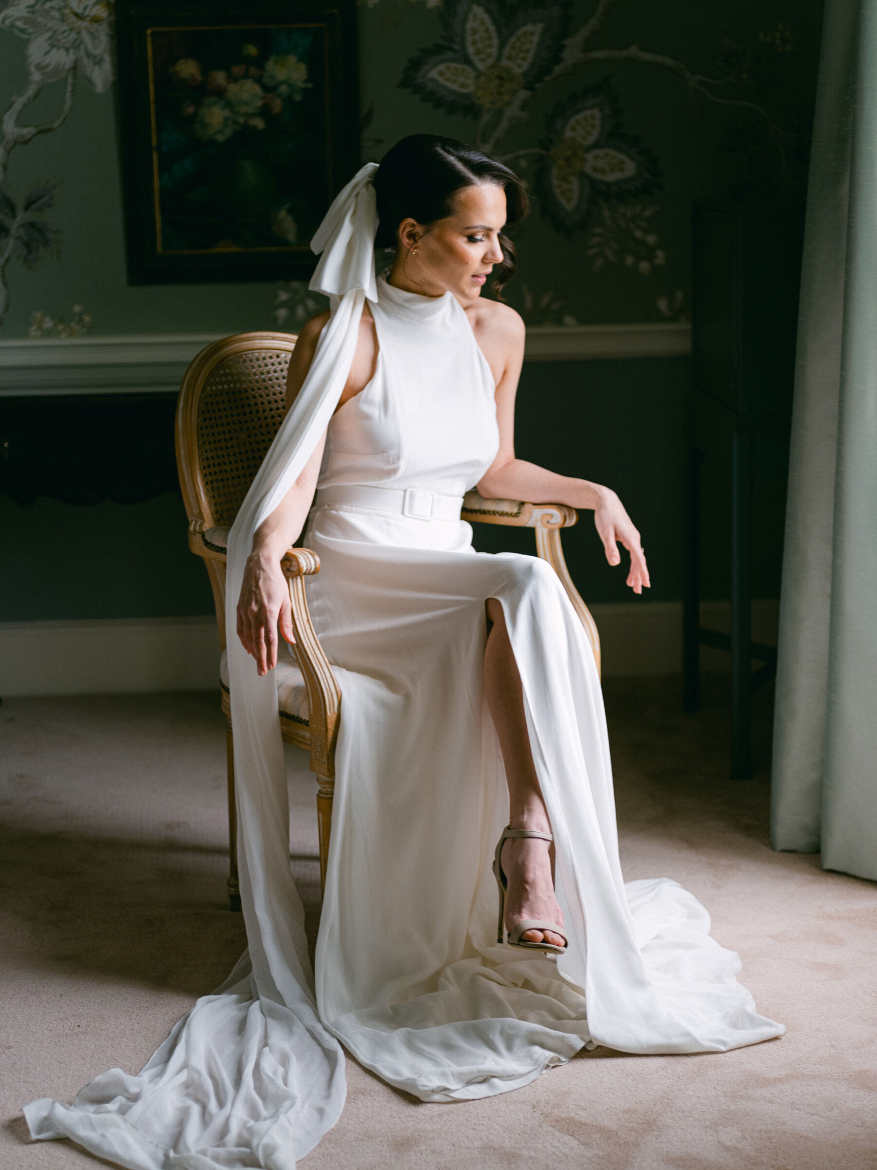 Bride seated wearing an elegant halterneck wedding dress and bow-veil.