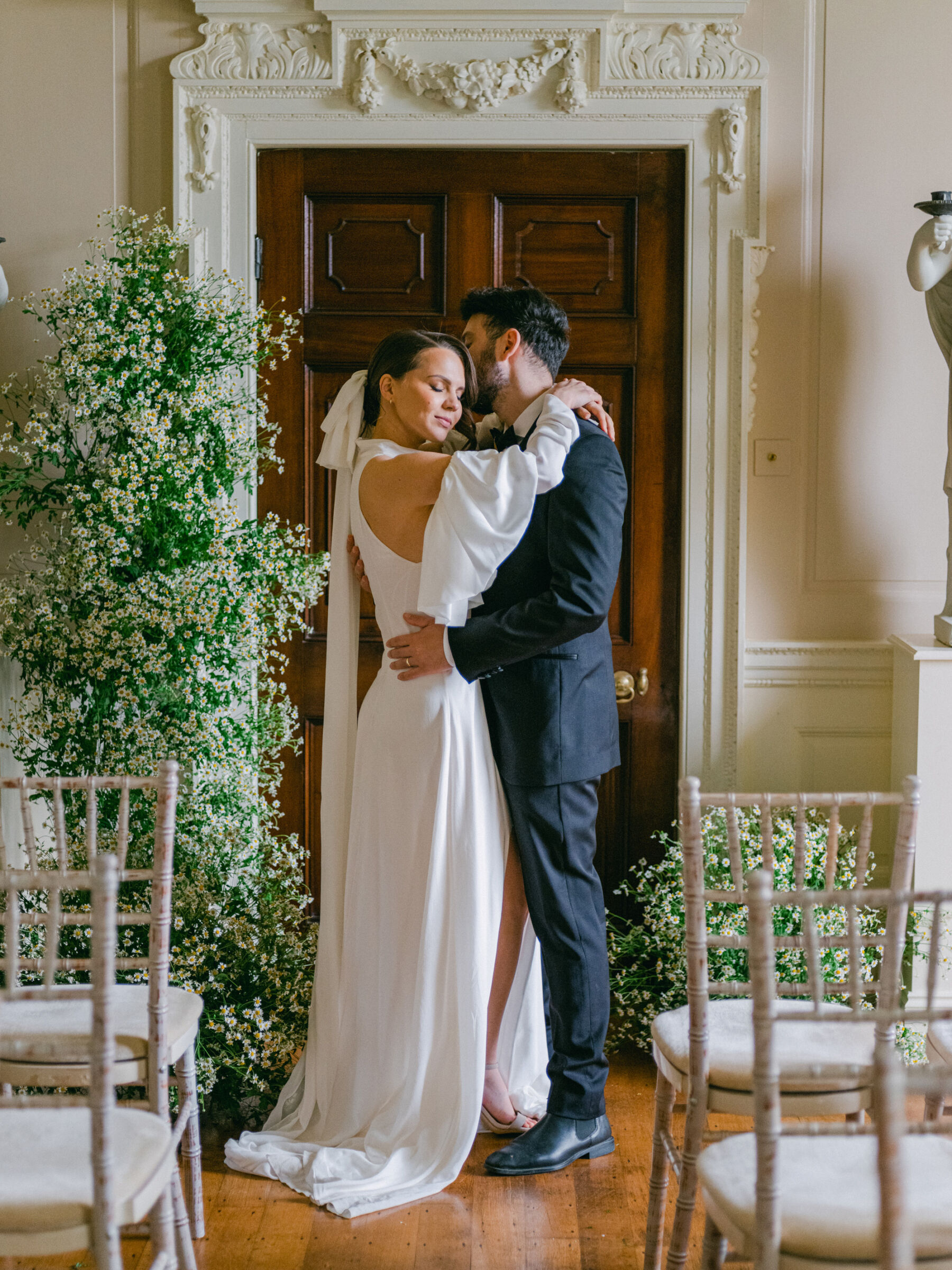 Celebrating Seasonal, British Grown Wedding Flowers With Flower & Fern at Findon Place 15 Bride and groom standing inside Findon Place next to a beautiful daisy floral arch.