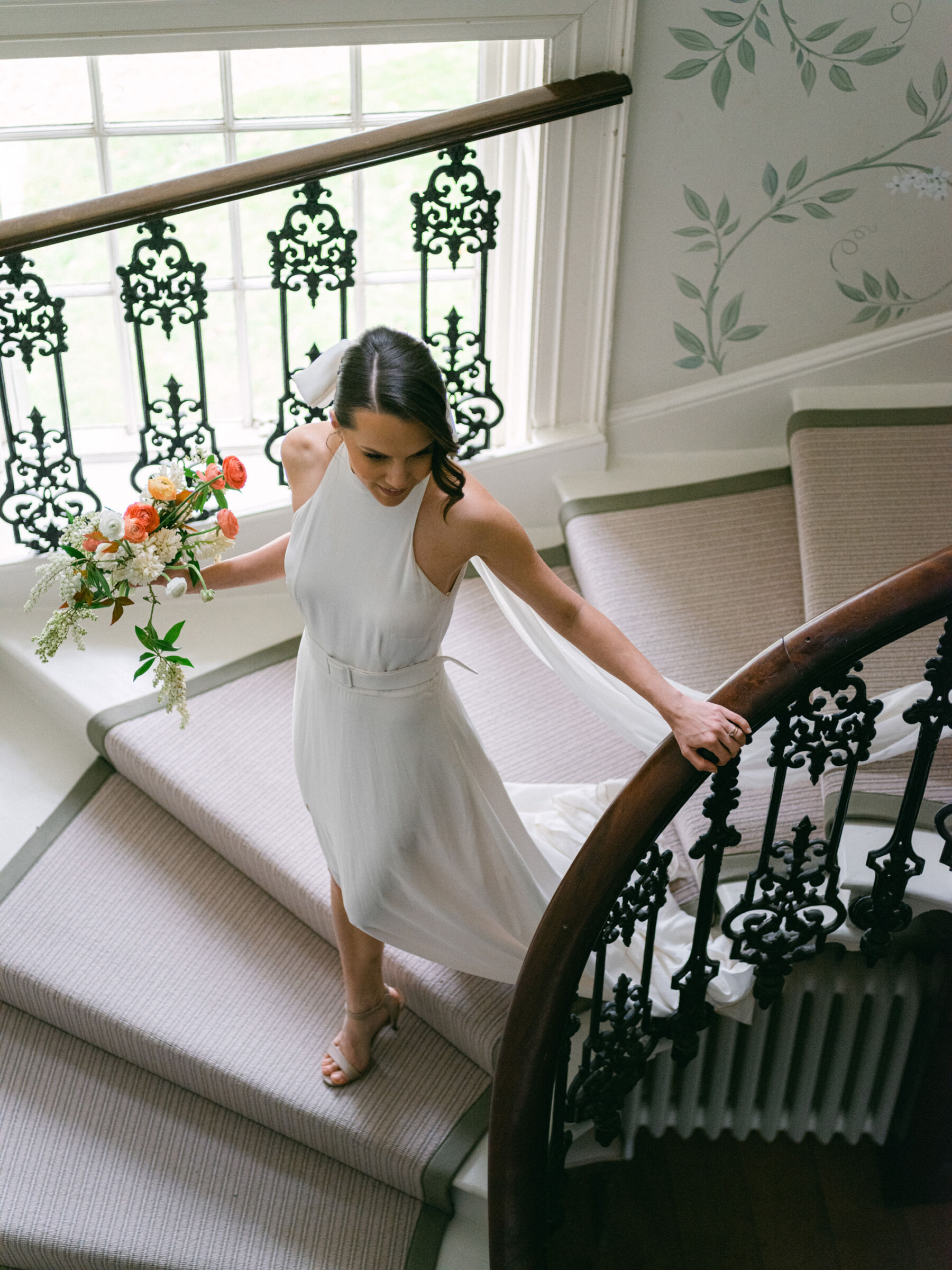 Bride descending down the staircase at Findon Place wearing an elegant halterneck wedding dress and bow-veil.