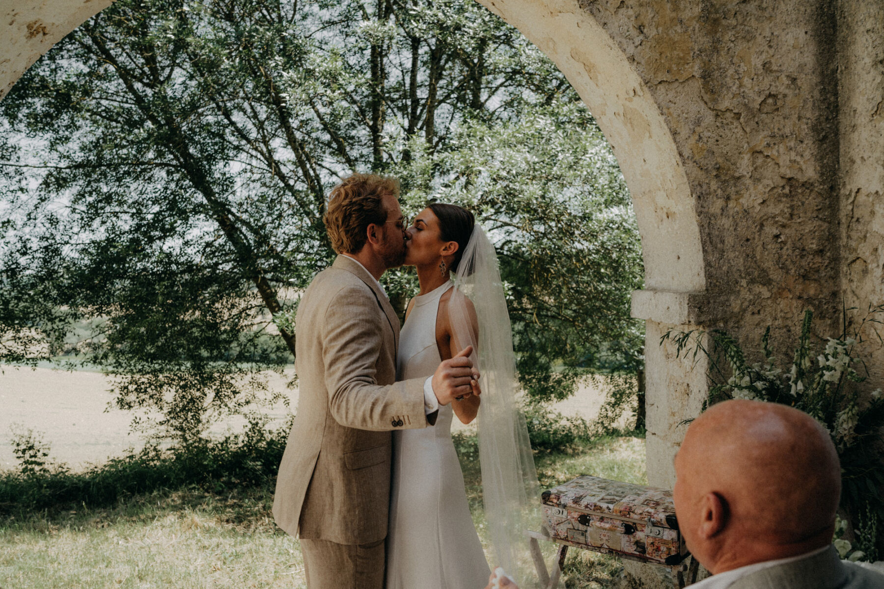 Bride and groom kissing at their outdoor wedding at a French chateau. Bride wears a halterneck silk wedding dress.