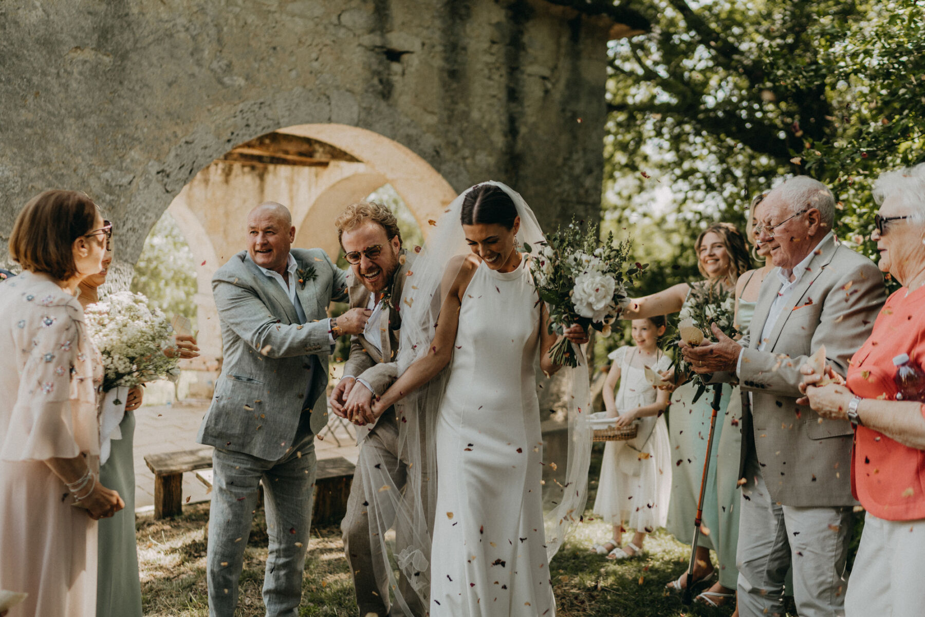 Bride and groom being showered with confetti. Bride wears a halterneck wedding dress and low bun.