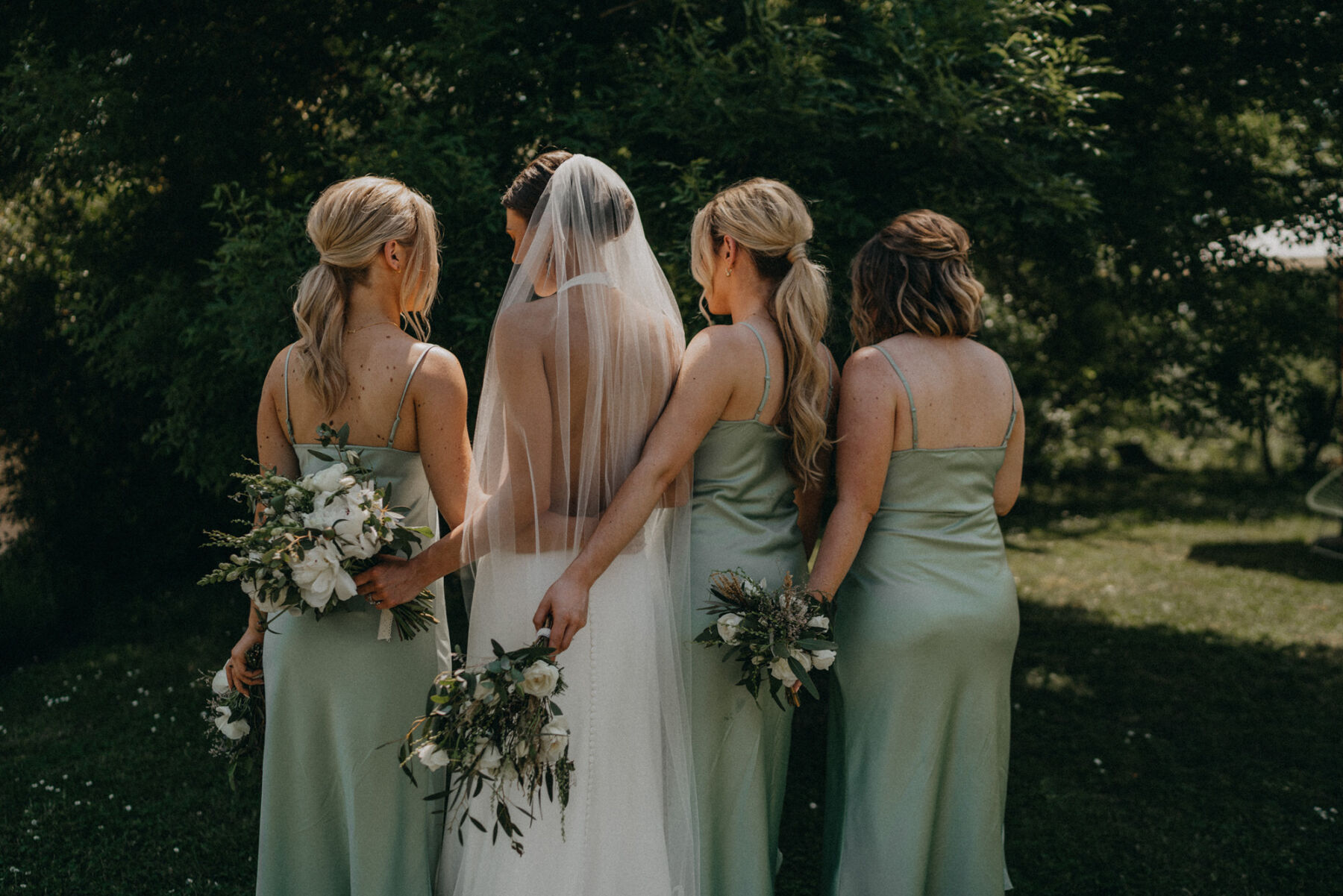 Shot of the back of a bride in a backless halterneck wedding dress with her bridesmaids in pale green satin dresses from Warehouse.