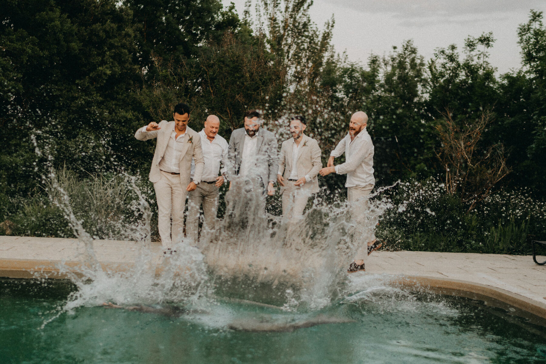 Groomsmen throwing the groom into a swimming pool. 