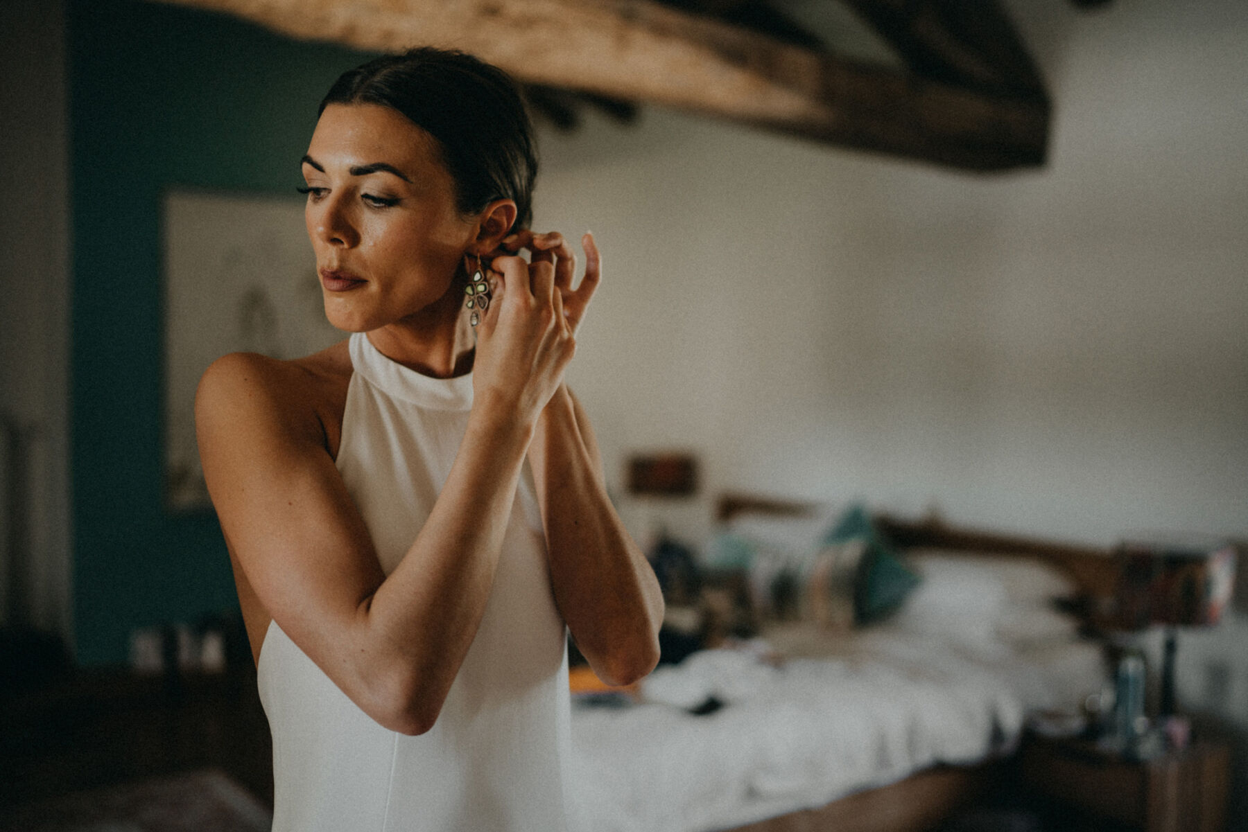 Emily in a Bespoke Halterneck Gown for her Elegant Chateau De Puissantut Wedding in South West France 8 Bride in a halterneck wedding dress and low bun putting her earrings in.