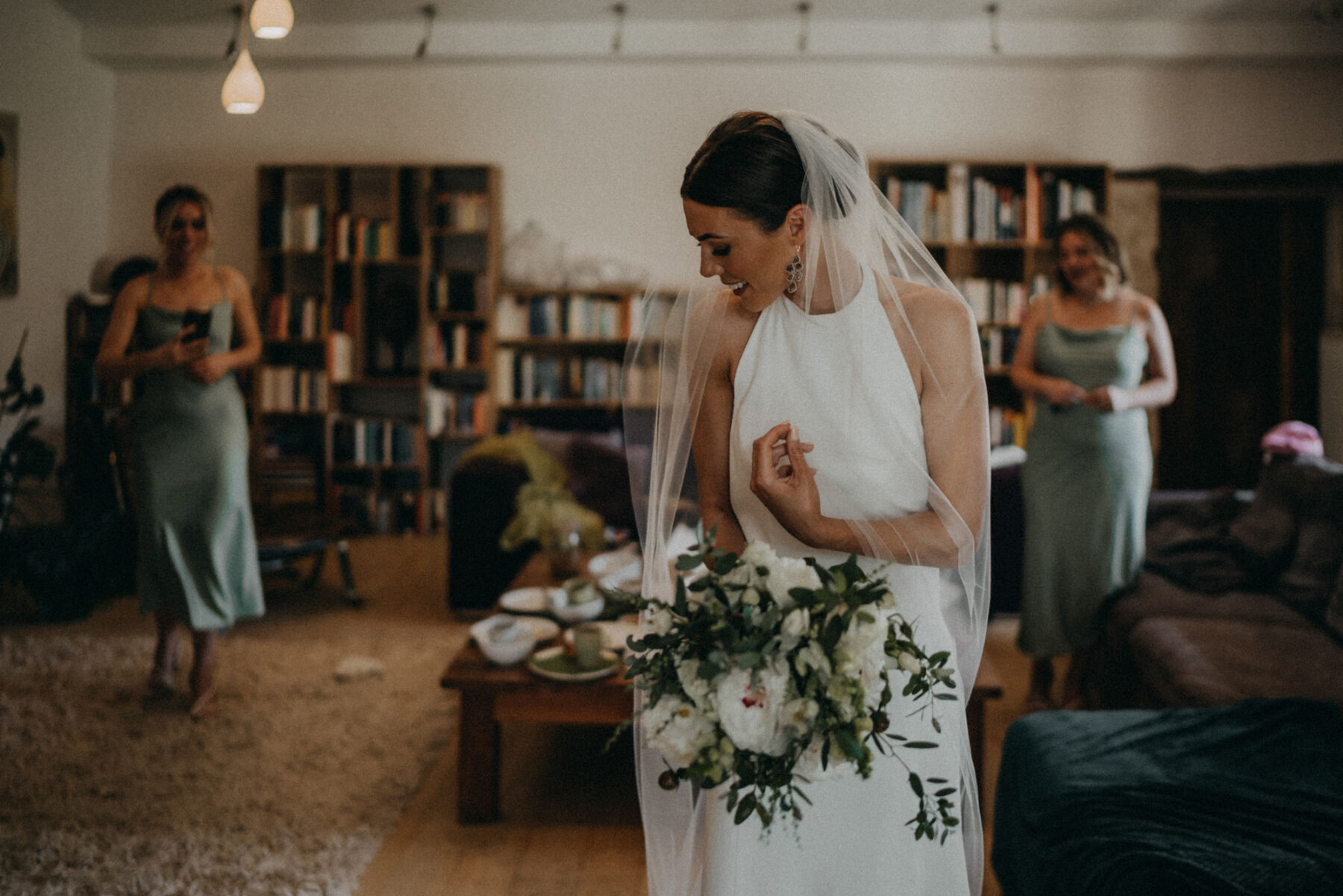 Bride in a halterneck wedding dress and embroidered veil carrying a white and green bouquet.
