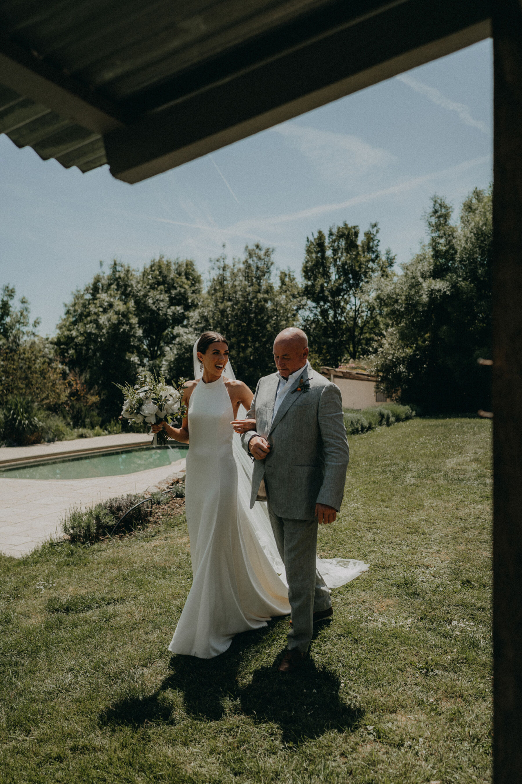 Bride in a halterneck wedding dress with her father walking to the ceremony.