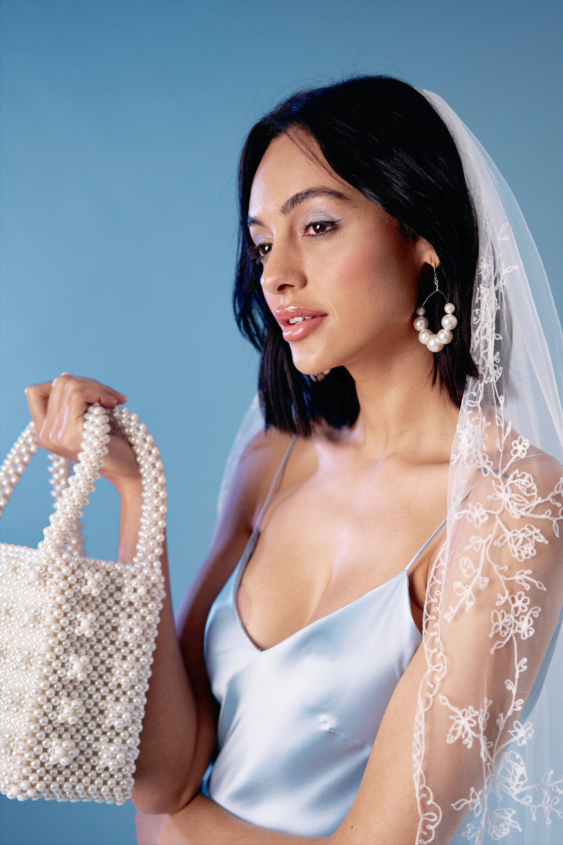 Pale blue wedding dress by Kate Beaumont. Bride carries a Shrimps pearl bag and wears and embroidered wedding veil.