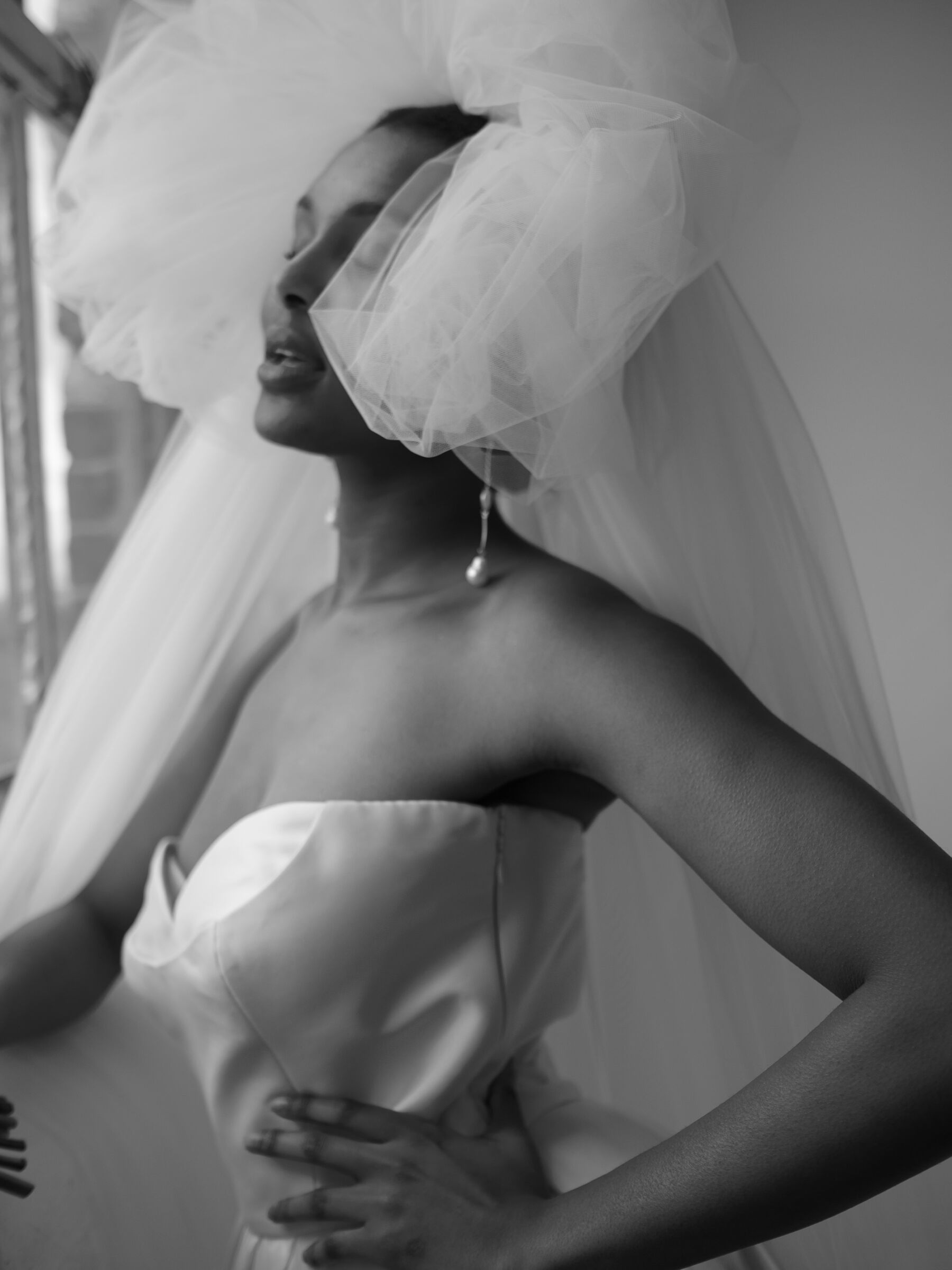 Black bride wearing a strapless dress, long pearl drop earrings & pouffy veil