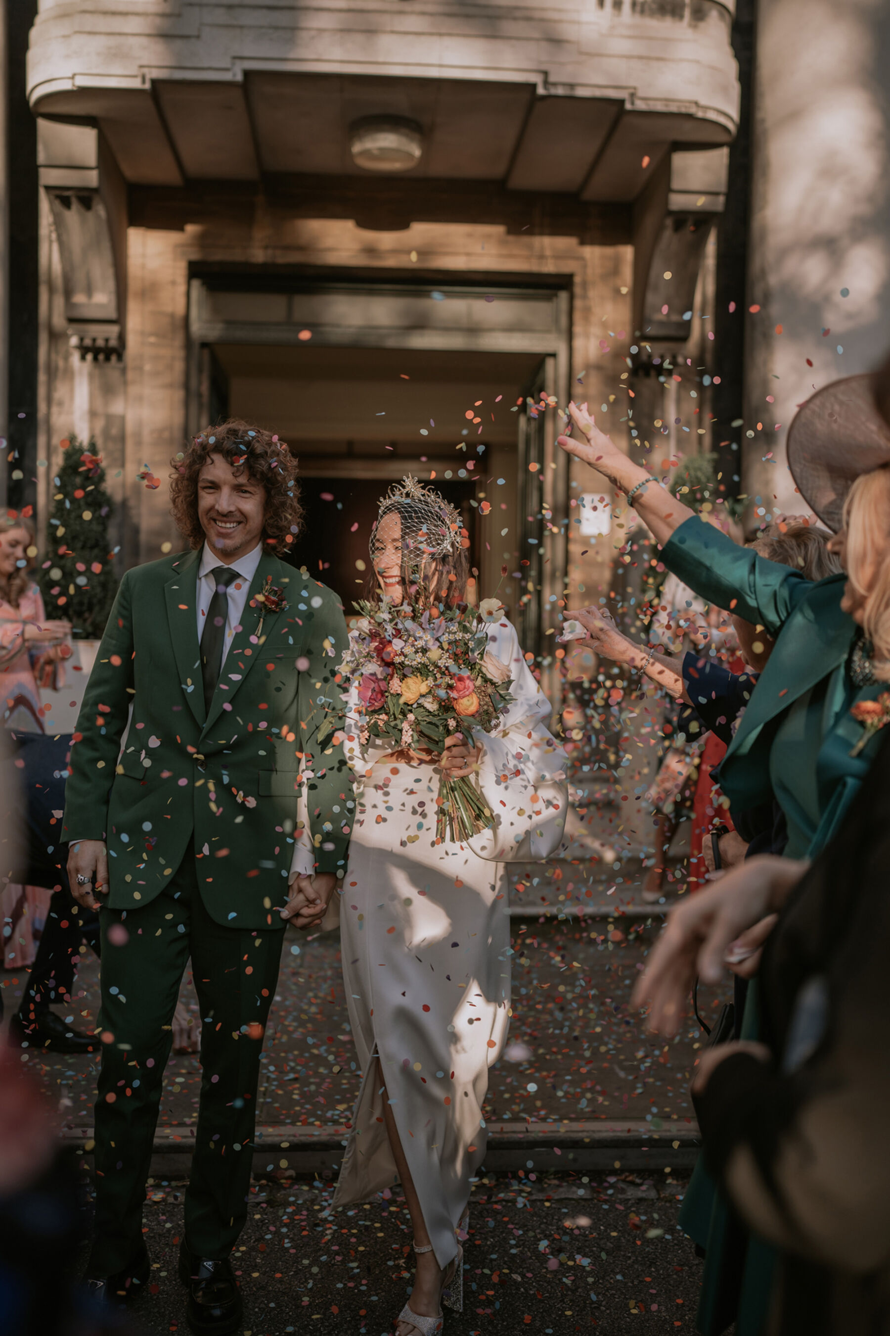 Bride and groom exiting the ceremony to a shower of confetti. Bride wears a birdcage veil and Bon Bride dress.