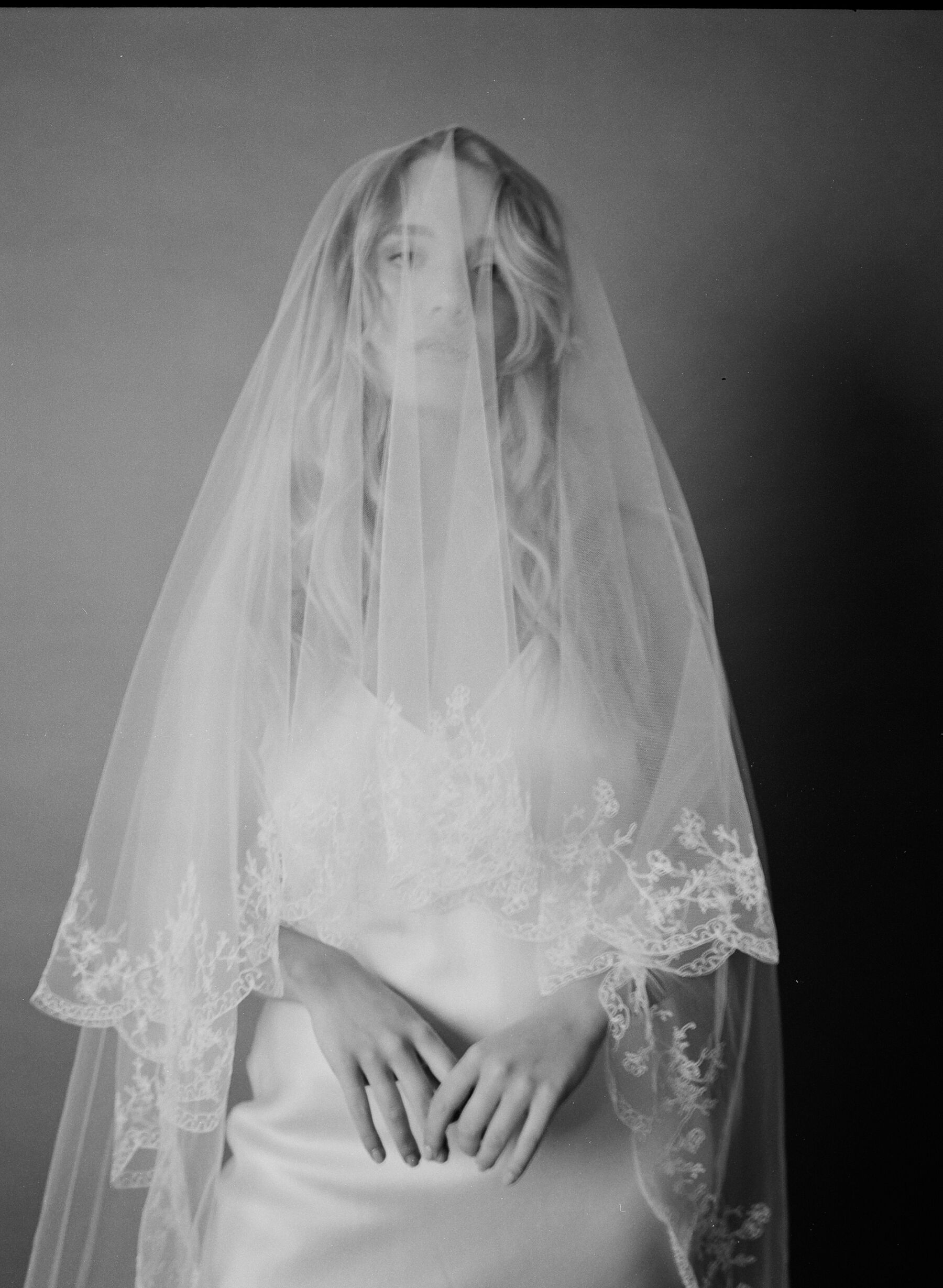 Black and white analogue photograph of an ethical wedding dress by British designer, Kate Beaumont and frilly edged wedding veil