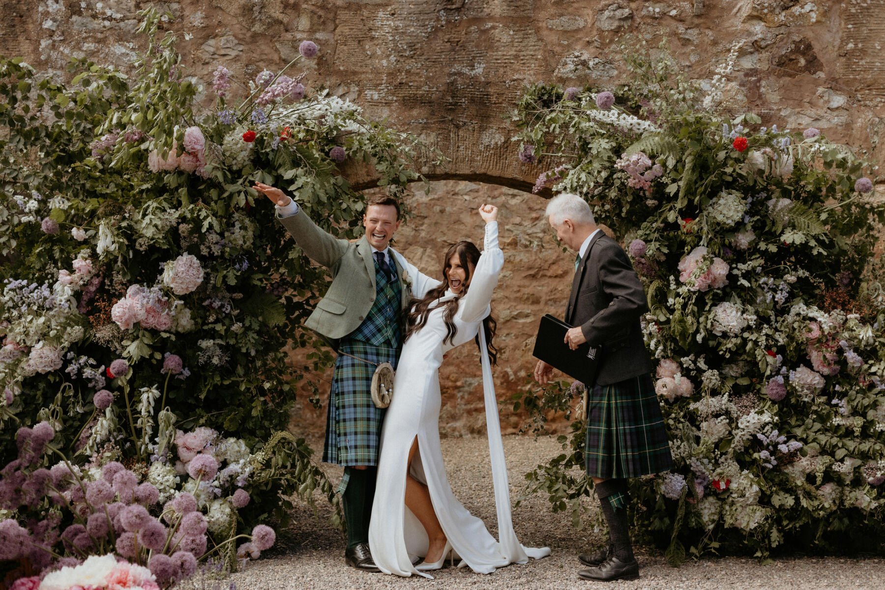 Bride and groom throwing fist punches by their floral backdrop after being declared man and wife