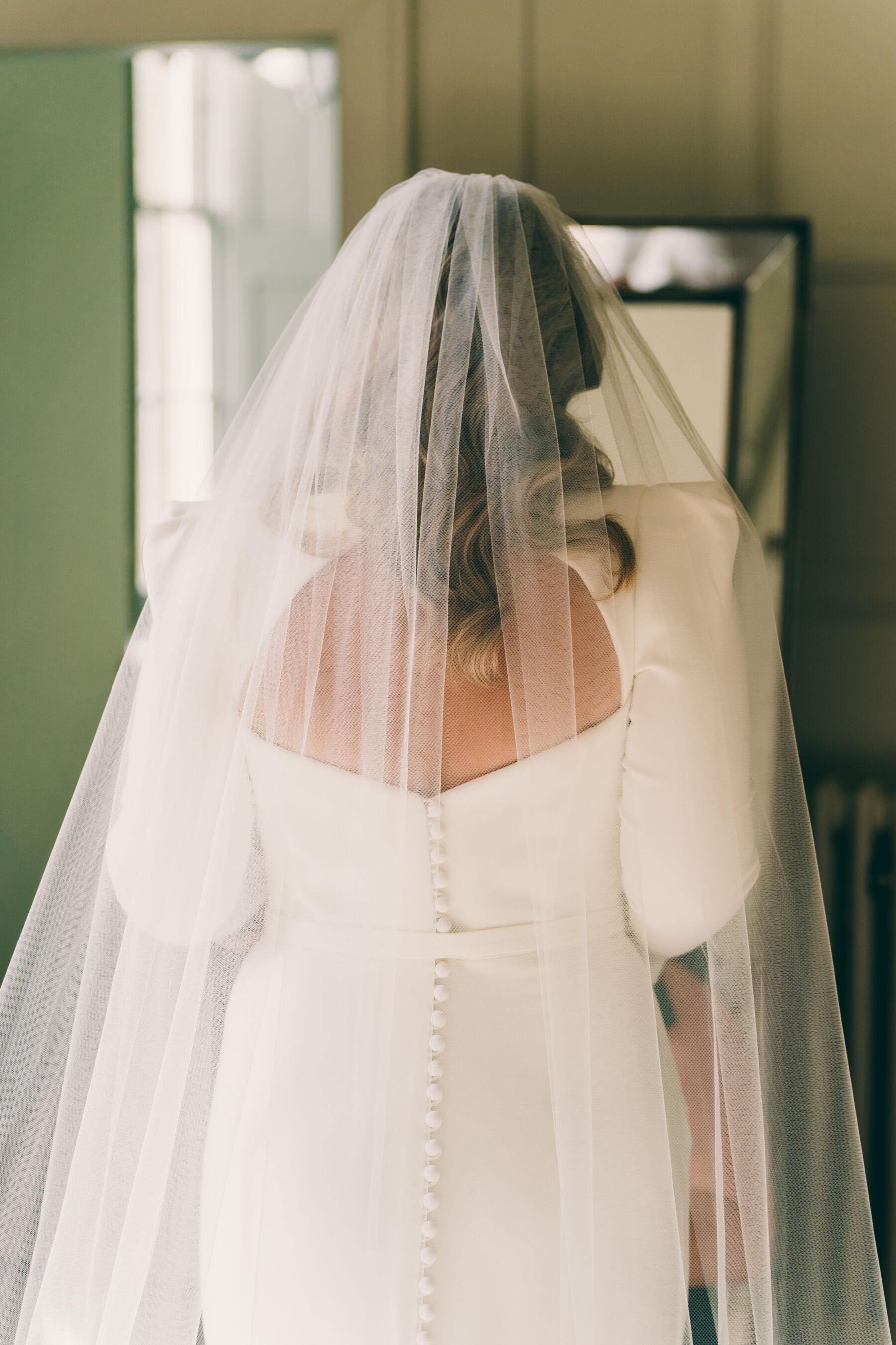 Plus size bride with her back to the camera wearing a Suzanne Neville dress and veil