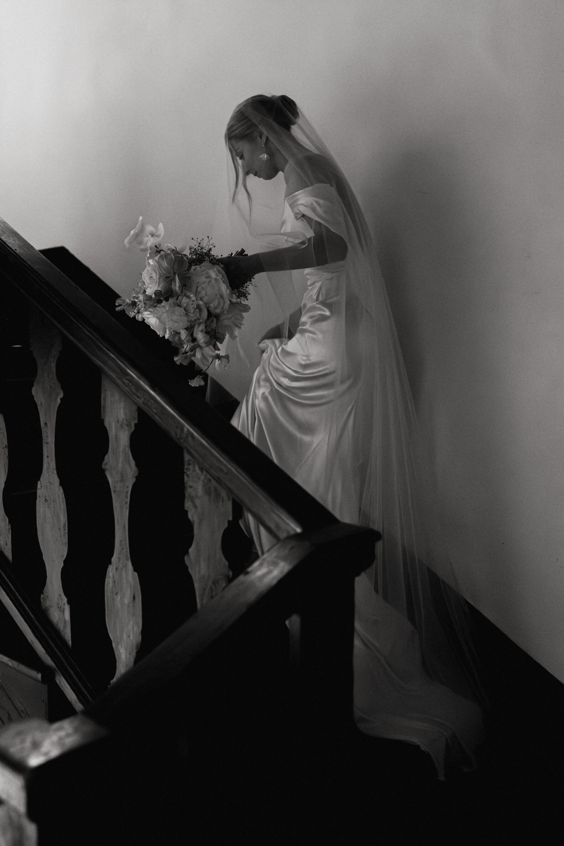 Elegant bride walking up a set of stairs in a silk Katherine Tash dress. She carries a large bouquet.
