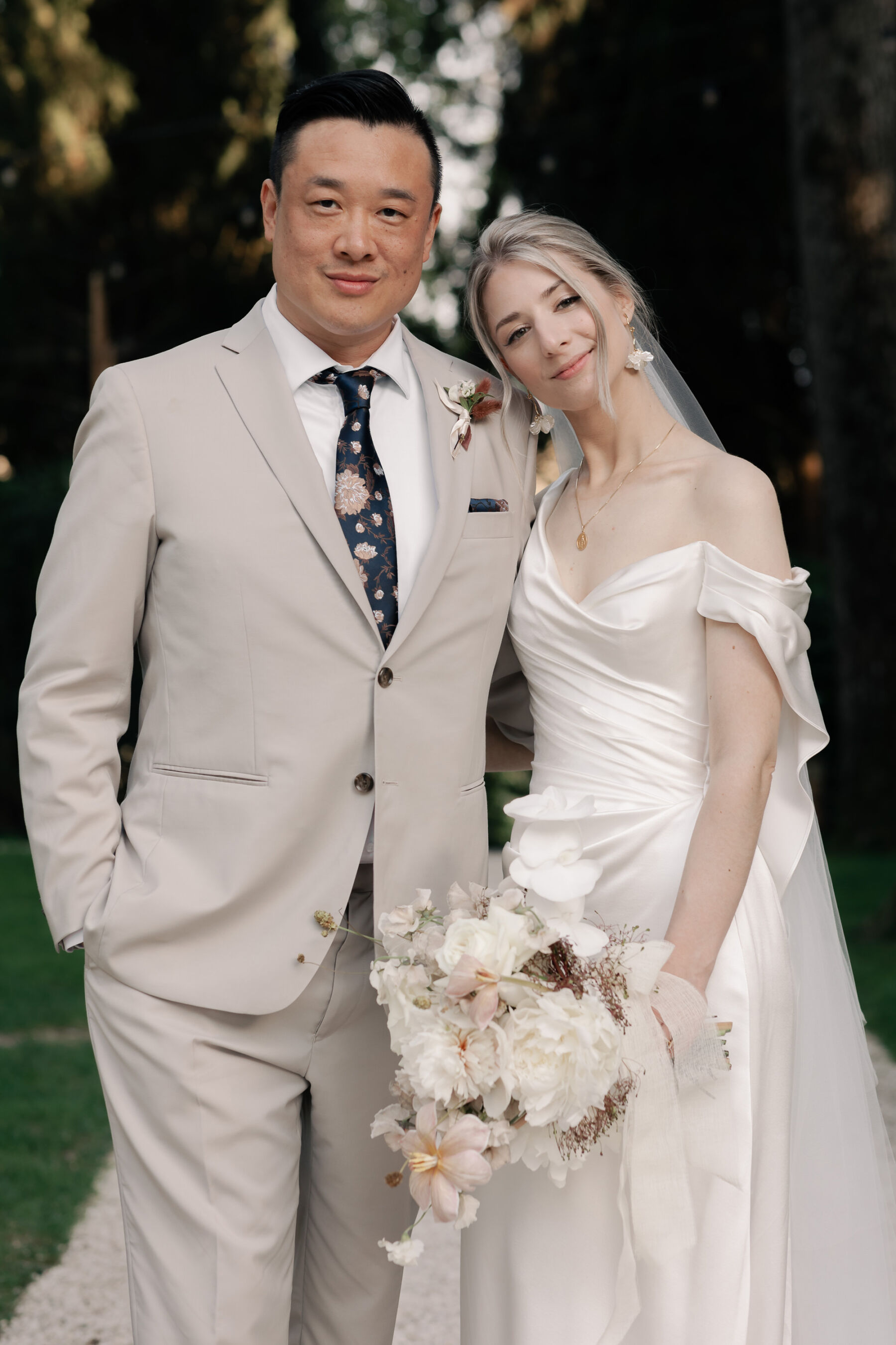 Groom in pale Indochino suit and floral tie. Bride leaning into him wearing an asymmetrical silk dress by Katherine Tash and carrying an organic and unstructured modern bridal bouquet. Bride wears her hair up in a simple French twist.